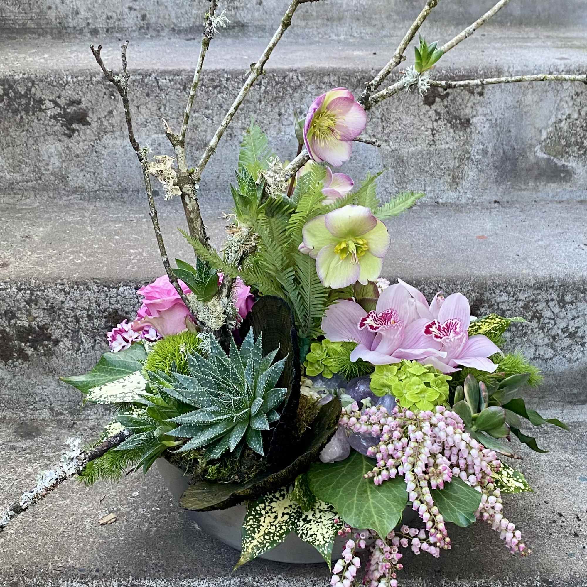 Mixed floral arrangement with orchids, roses, succulents, and branches in a low container