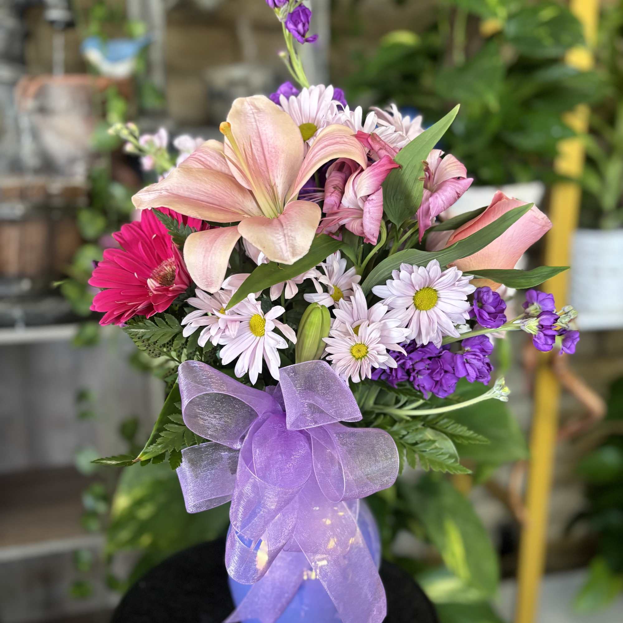 Pink and purple mixed bouquet in a lavender vase with a sheer bow
