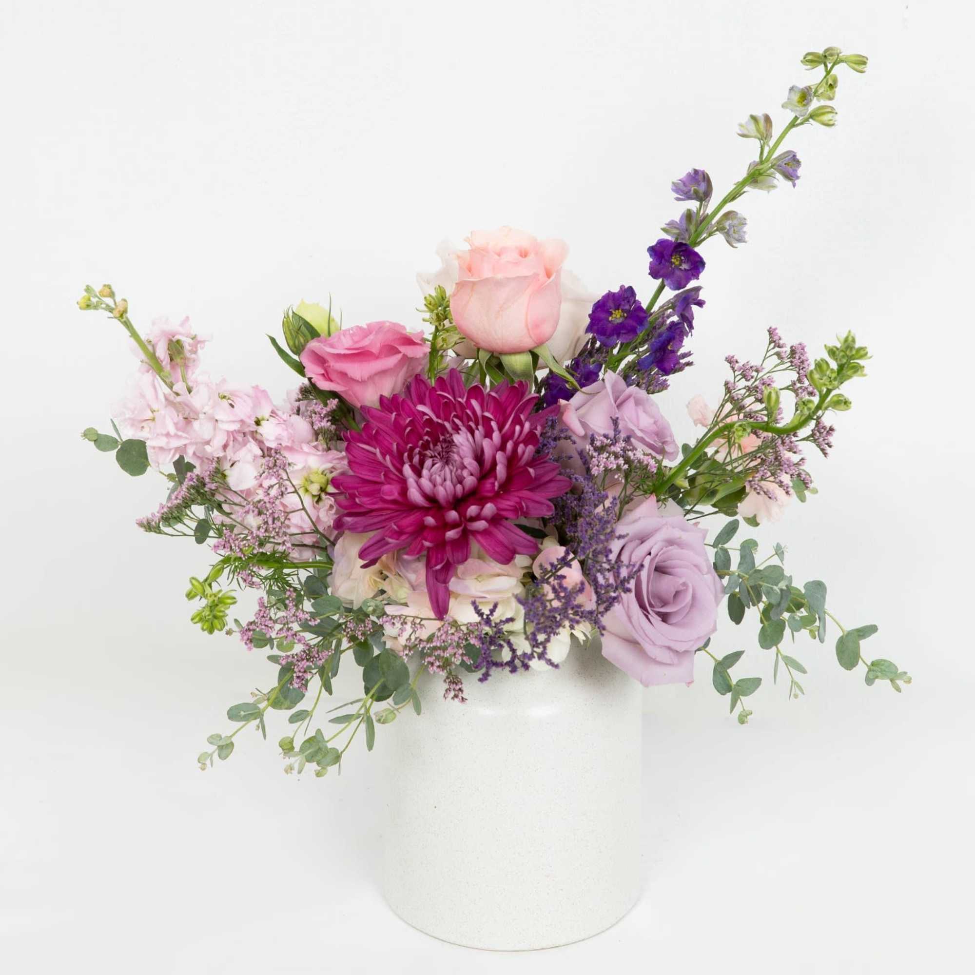 Arrangement of pink and purple flowers including roses and a mum in a white ceramic vase
