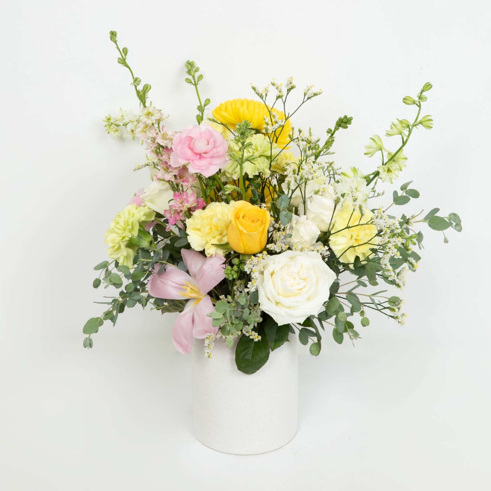 Mixed arrangement of yellow, white, and pink flowers in a white cylindrical vase