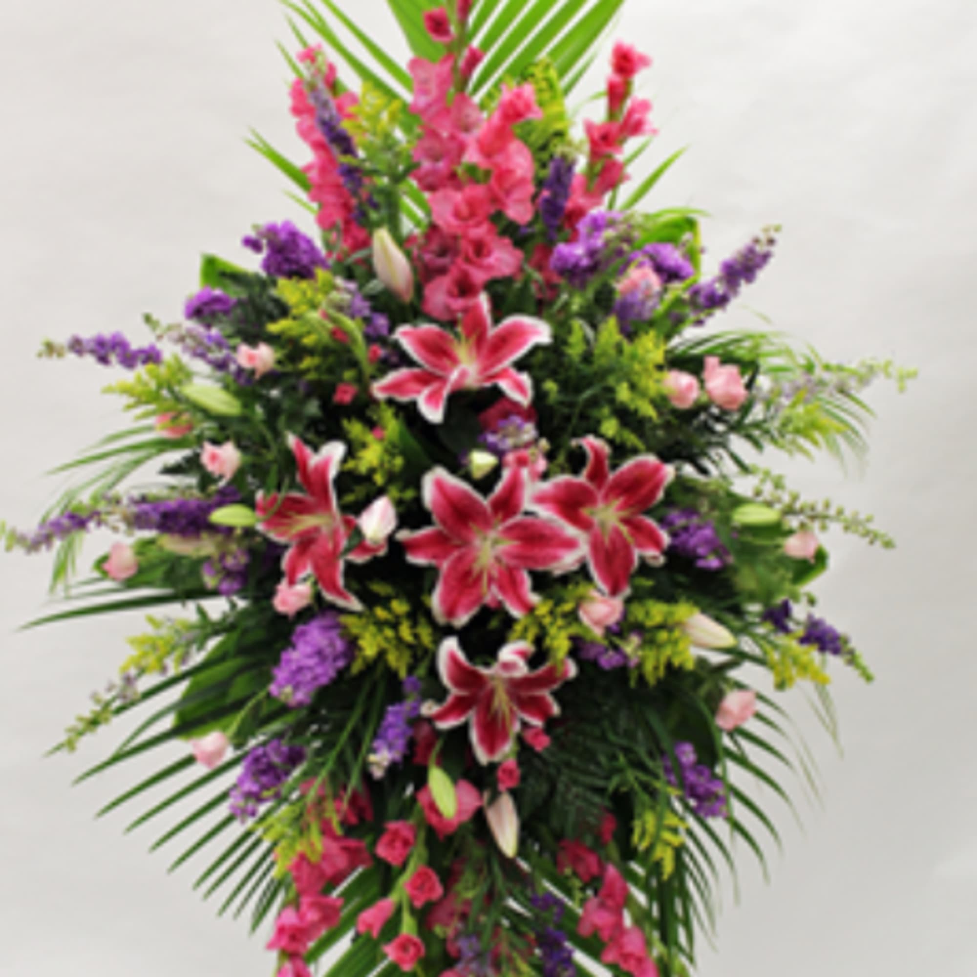 Tall standing spray of pink lilies and mixed flowers with palm fronds