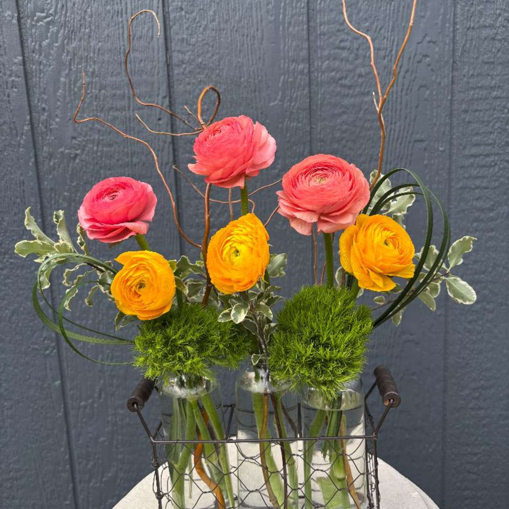Bright, cheerful ranunculus seem to dance above a collection of charming glass