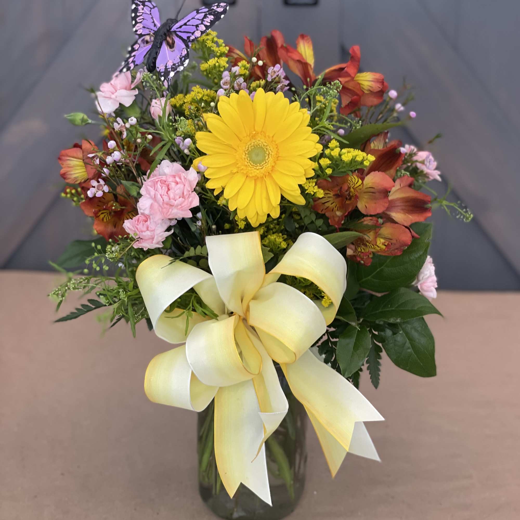 Mixed bouquet in a glass vase with a yellow ribbon and butterfly pick