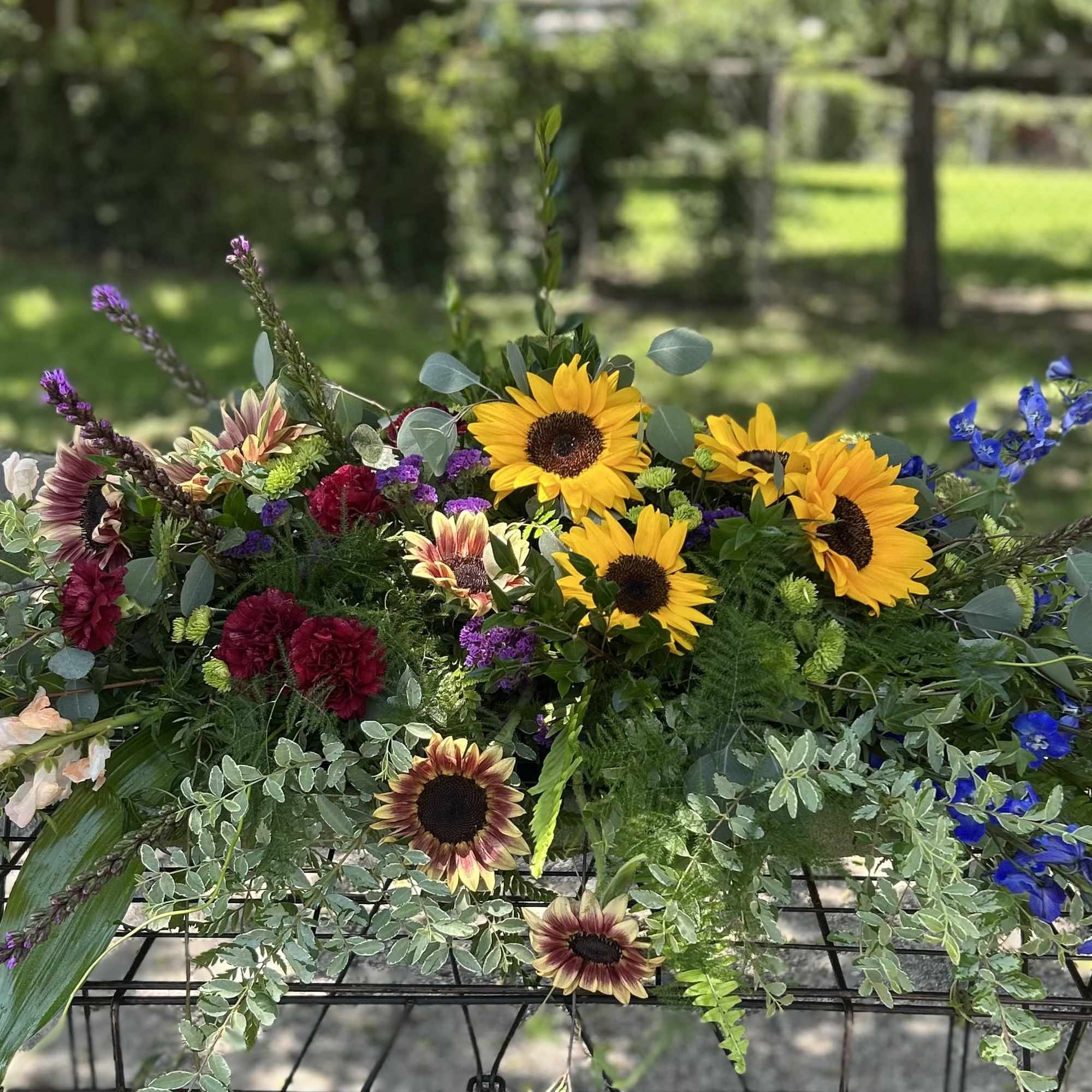 Mixed bouquet with sunflowers, blue delphinium, and burgundy blooms