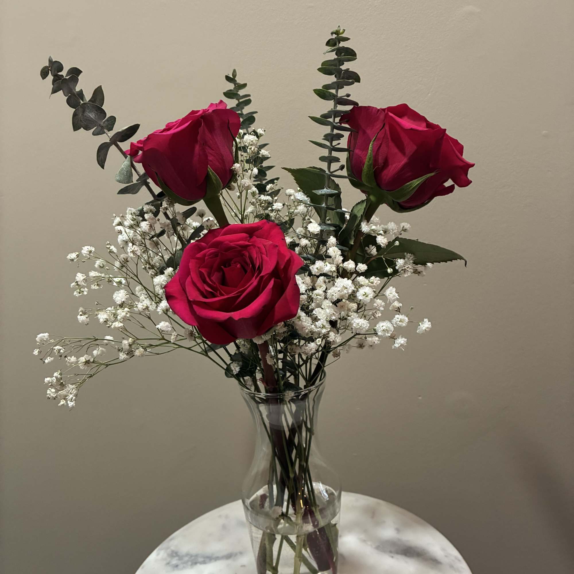 Three fresh roses arranged with greenery in a petite vase. Perfect for
