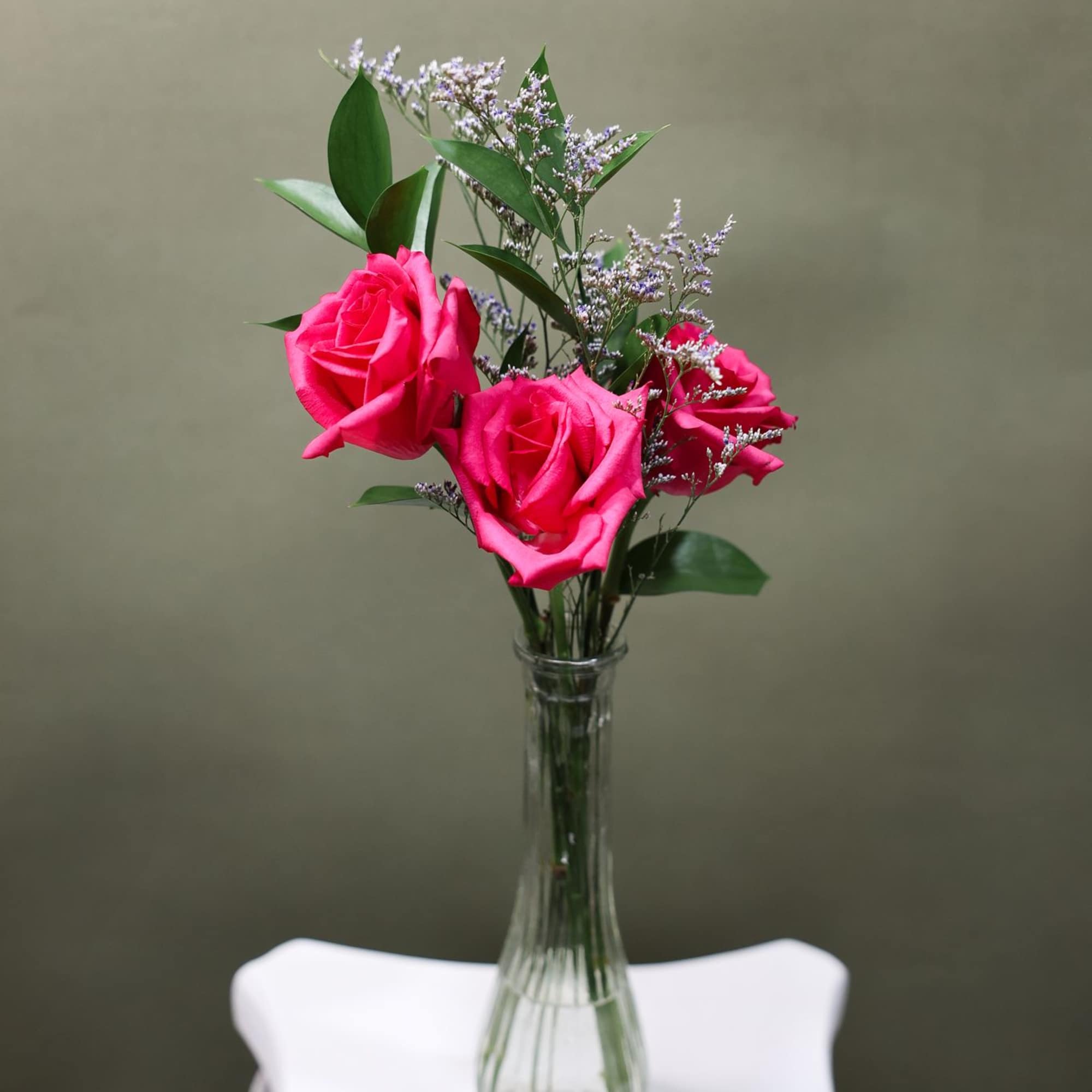 Three fresh roses arranged with greenery in a petite vase. Perfect for