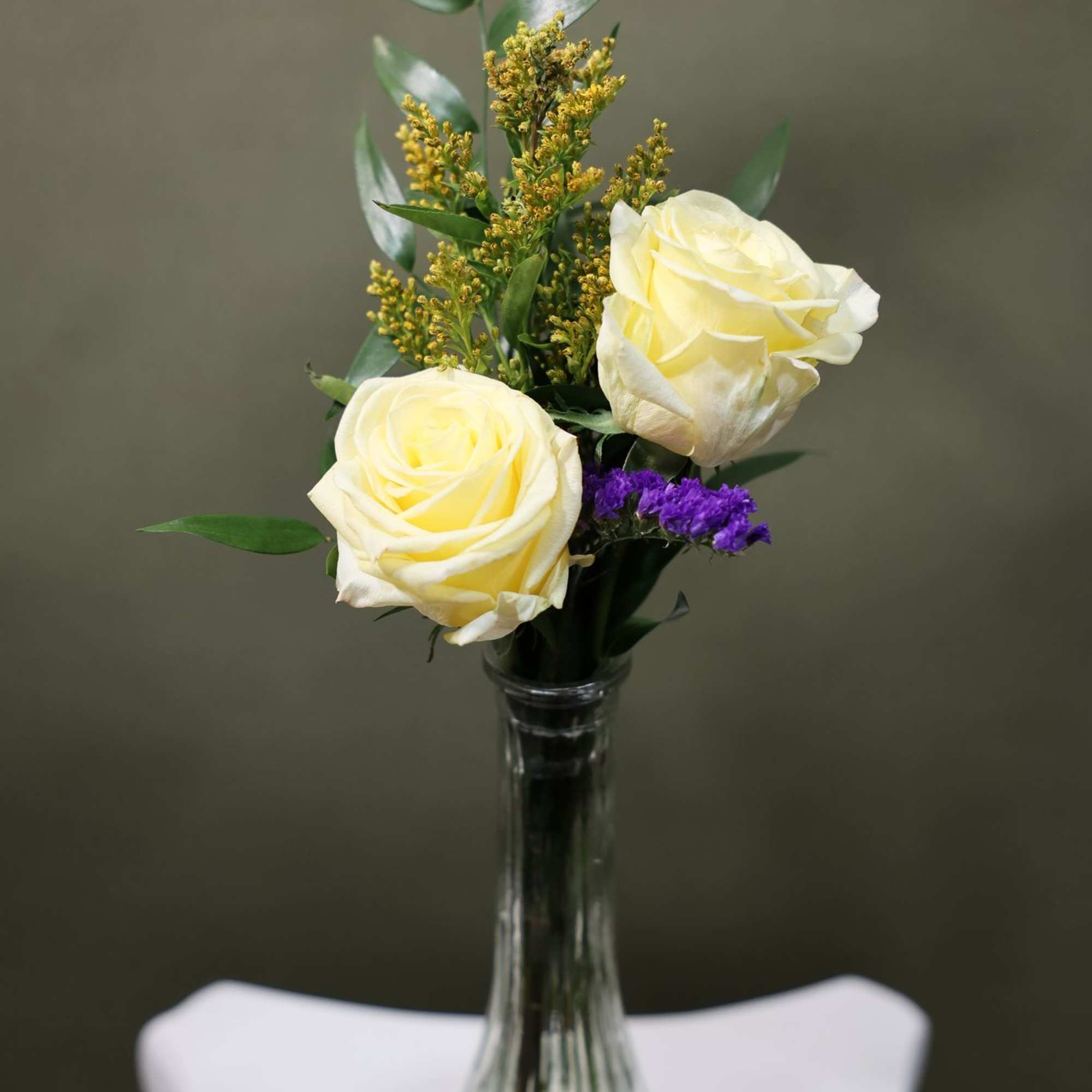 Two beautiful roses arranged with fresh greenery in a petite vase. This