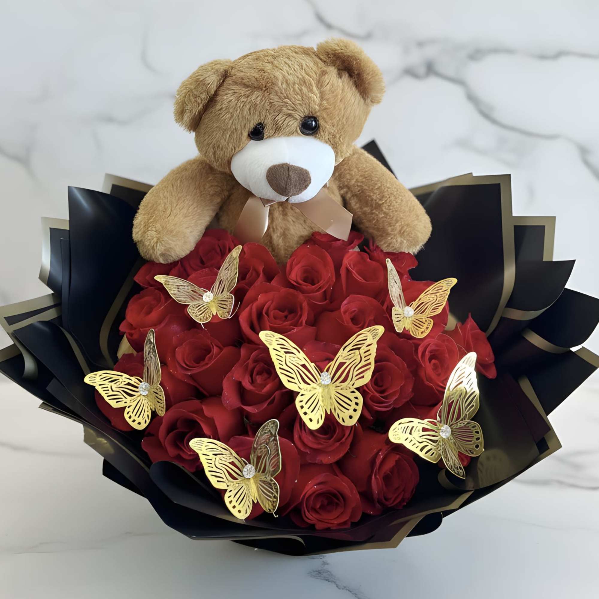 Teddy bear sitting on a bouquet of red roses with gold butterfly decorations