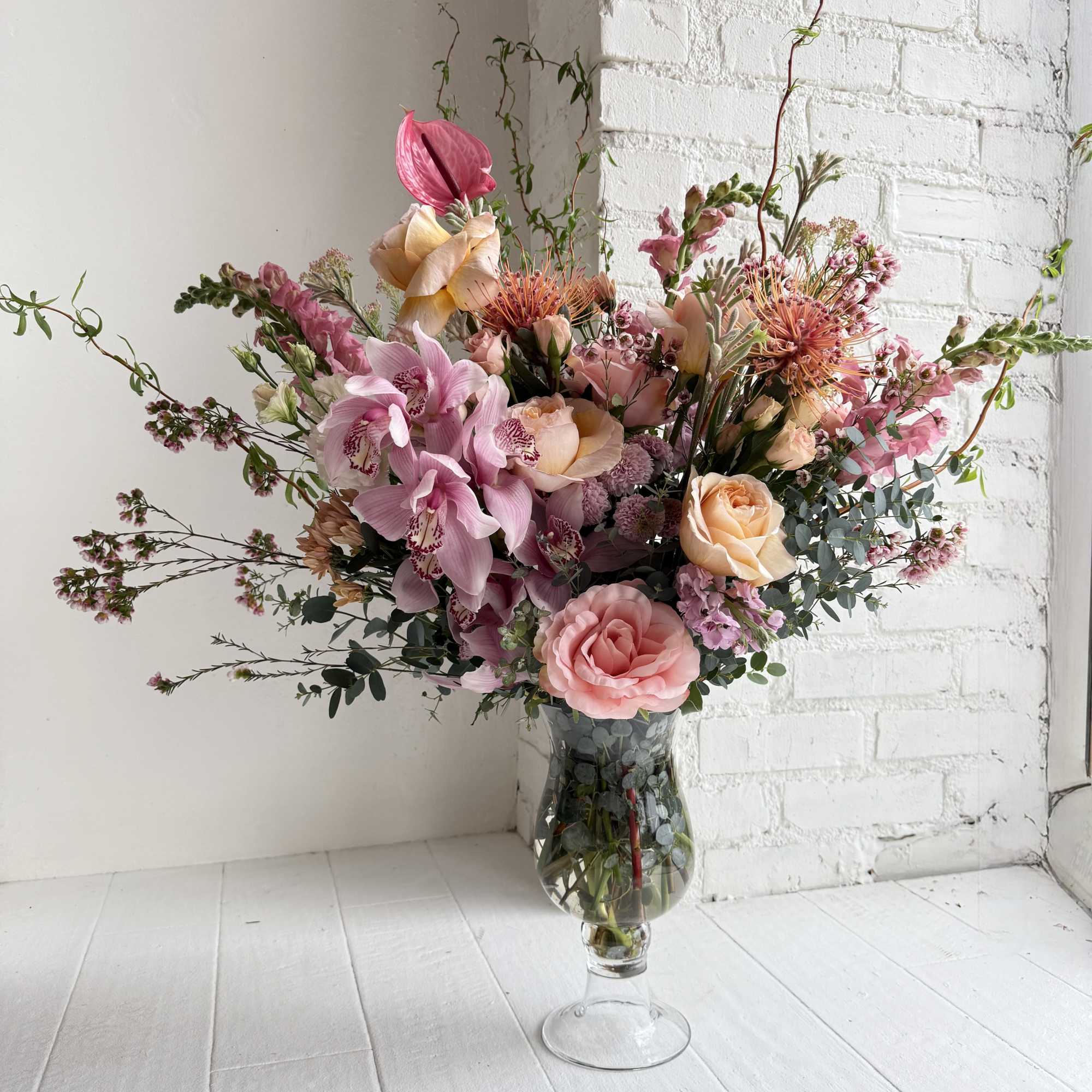 A stunning tall arrangement consisting of light pinks, peach and light foliage.