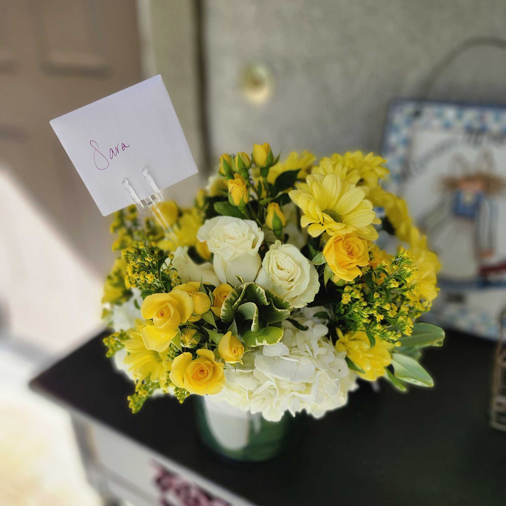 This white and yellow arrangement includes cream roses, button mums, and ranunculuses.