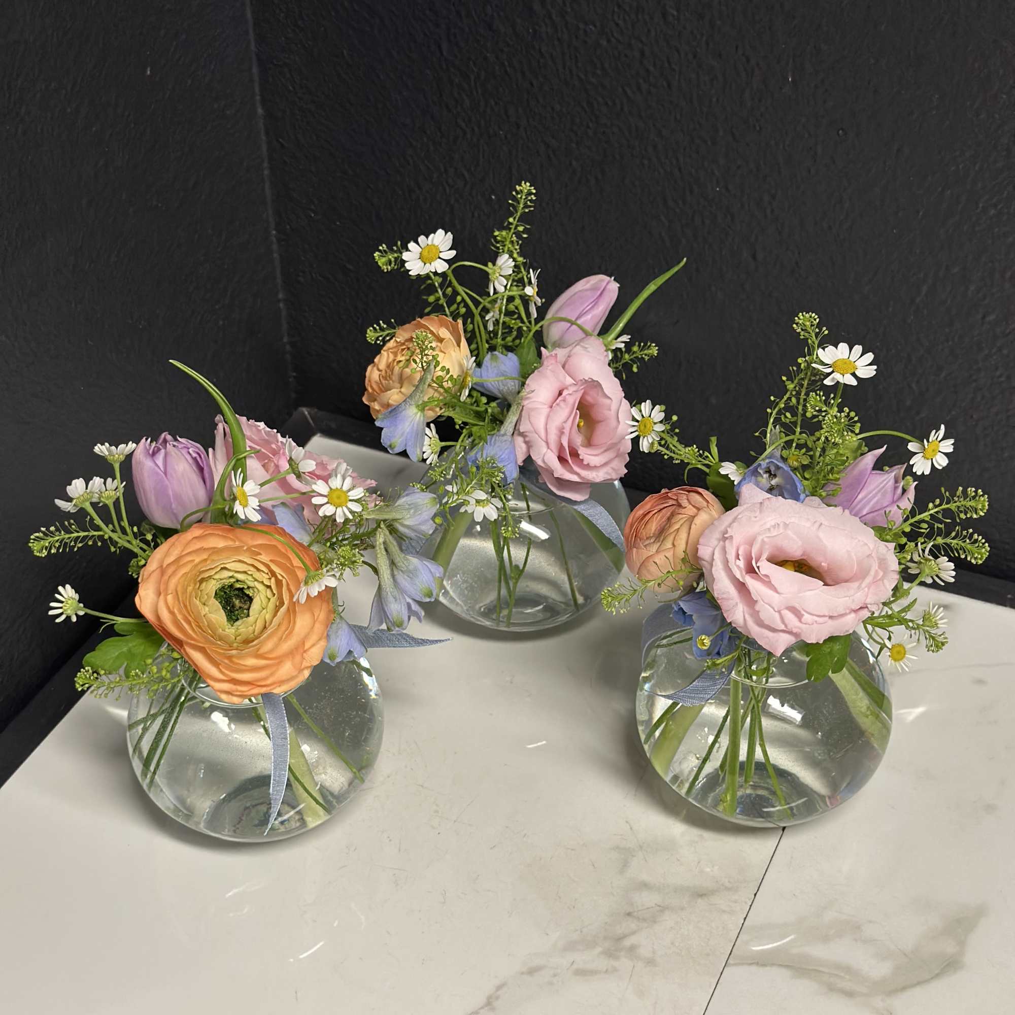 A trio of budvases filled with seasonal blooms in soft pastel shades.