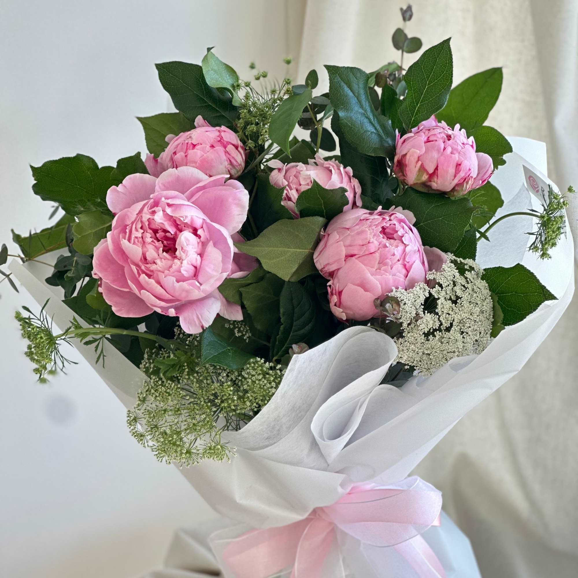 A round bouquet of peonies with plenty of greenery and fillers, wrapped