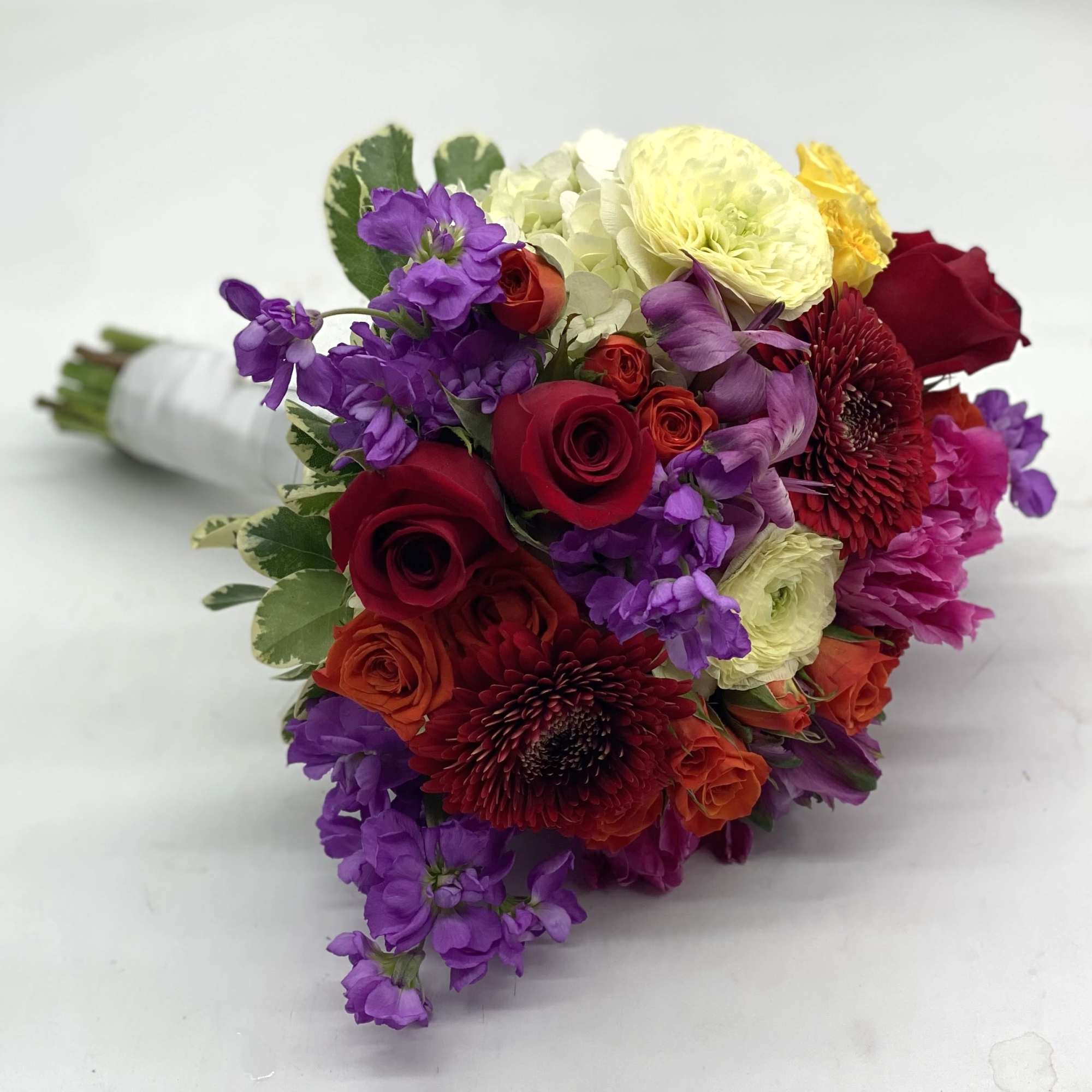 A lush mix of red roses, pale yellow ranunculus, red gerbera daisies
