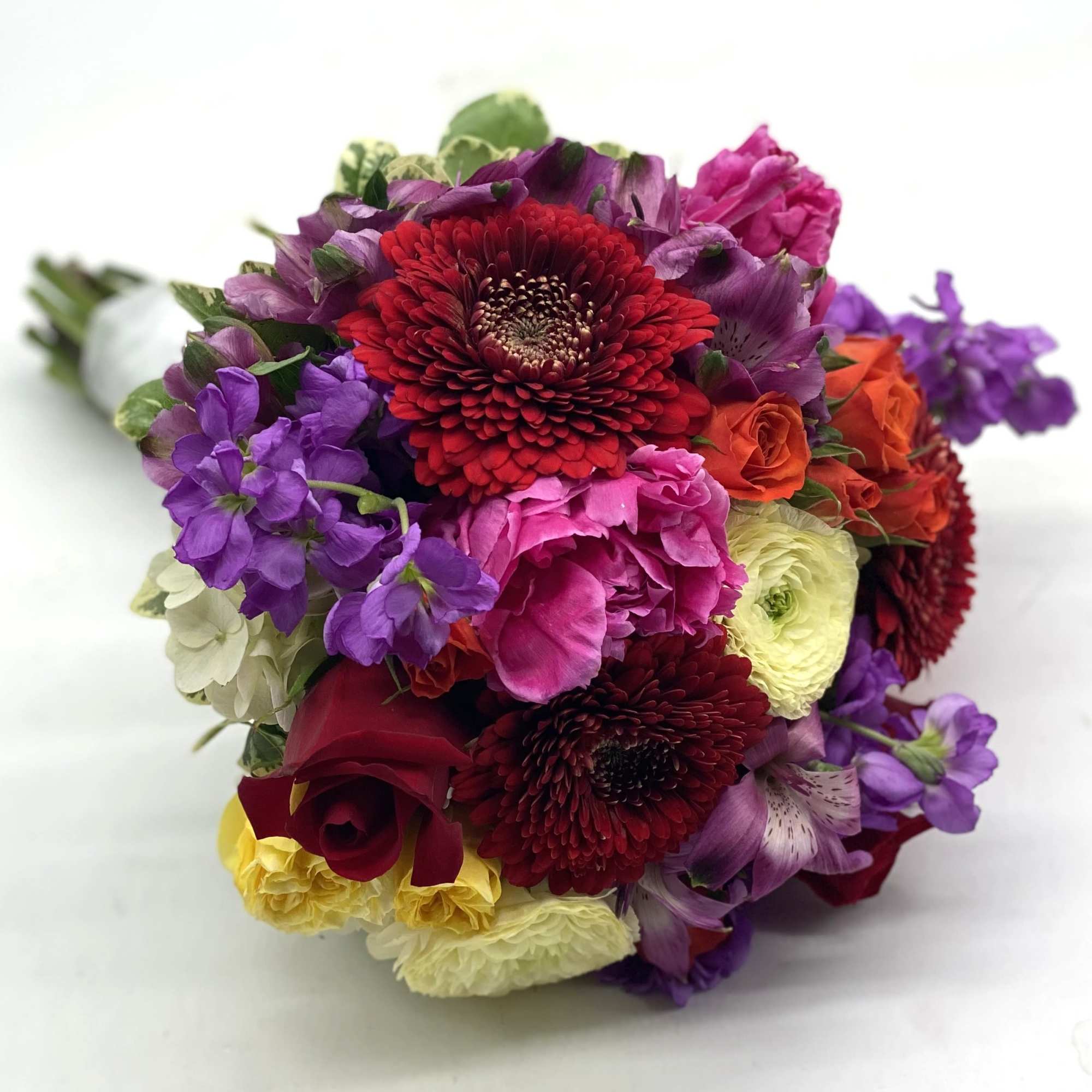 A lush mix of red roses, pale yellow ranunculus, red gerbera daisies