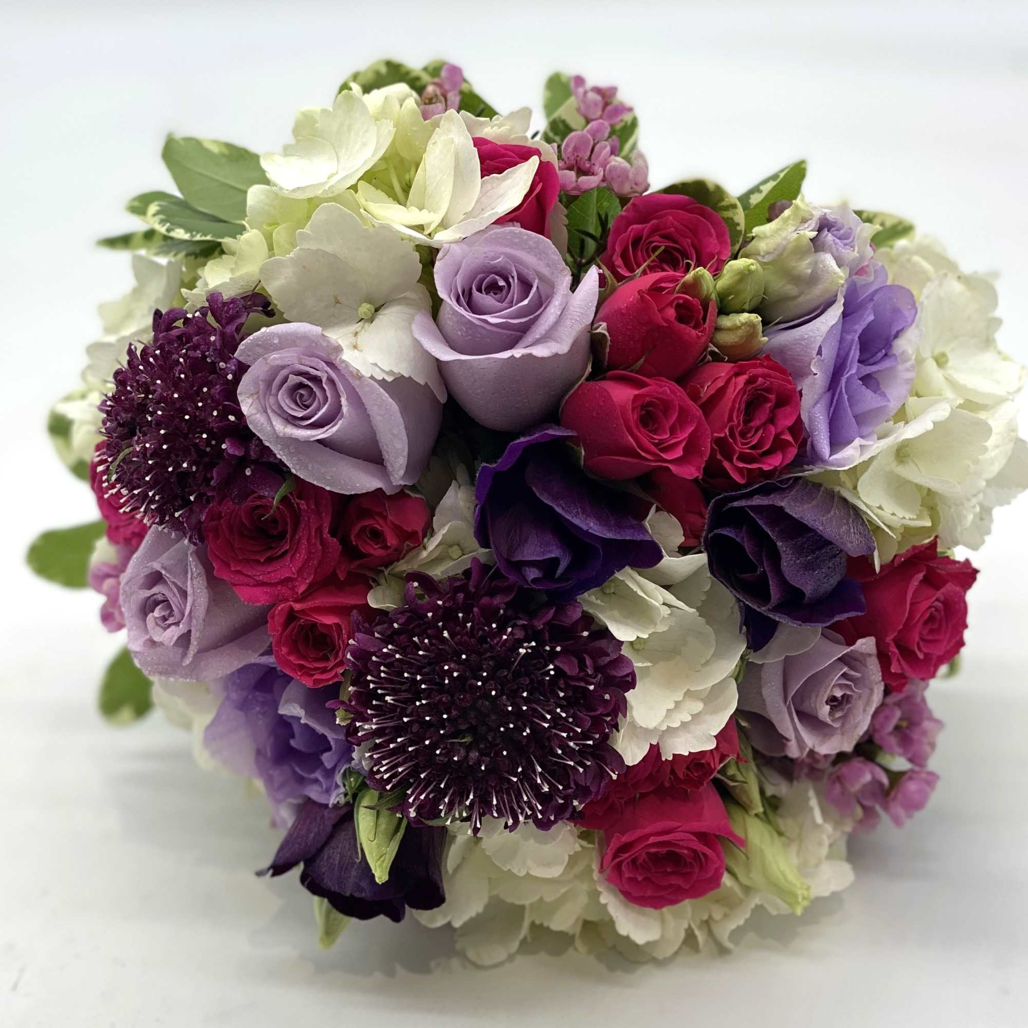 Round bouquet of lavender, fuchsia, purple, and white flowers in a compact hand-tied design
