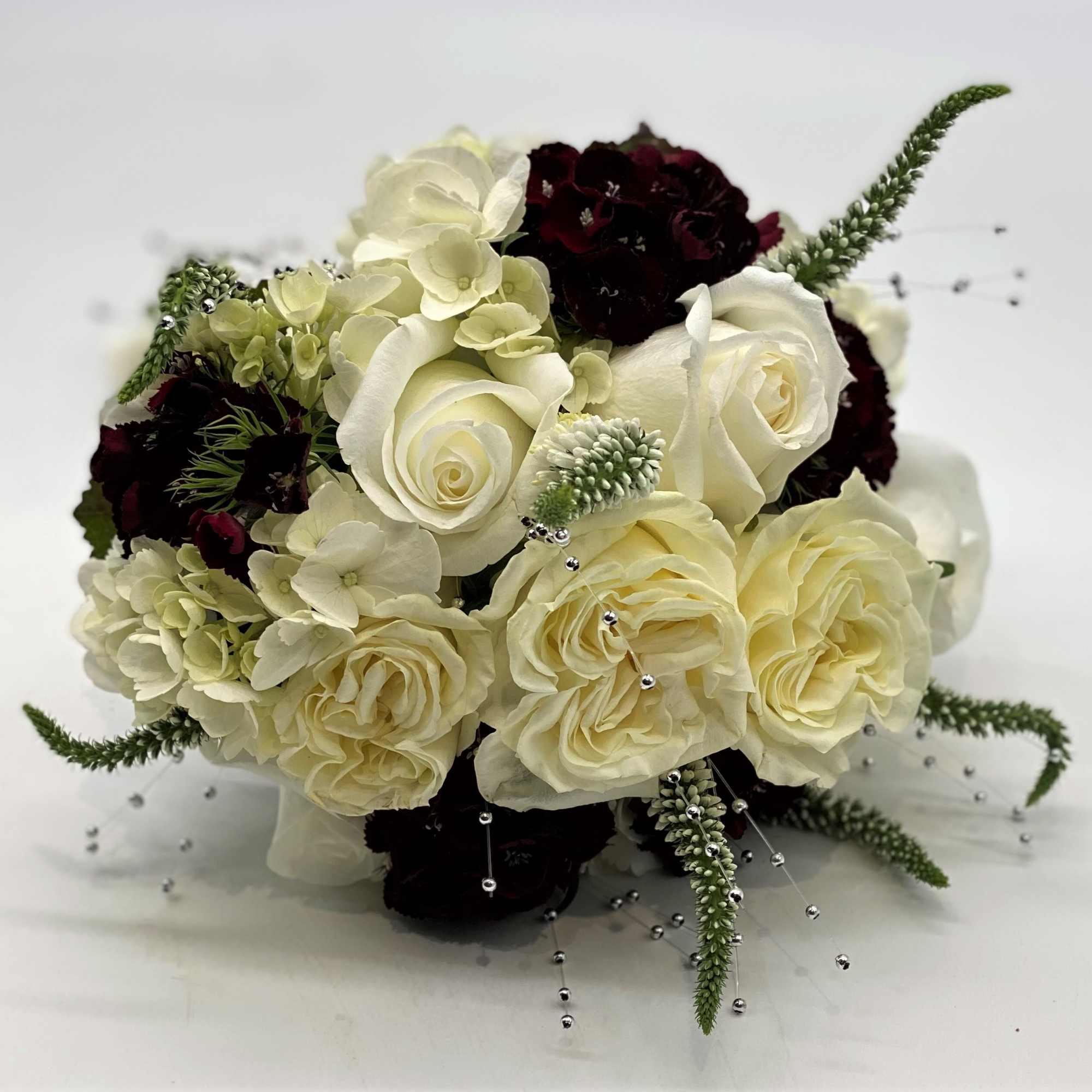 Round bouquet of ivory roses and hydrangeas with dark burgundy accents and bead sprays