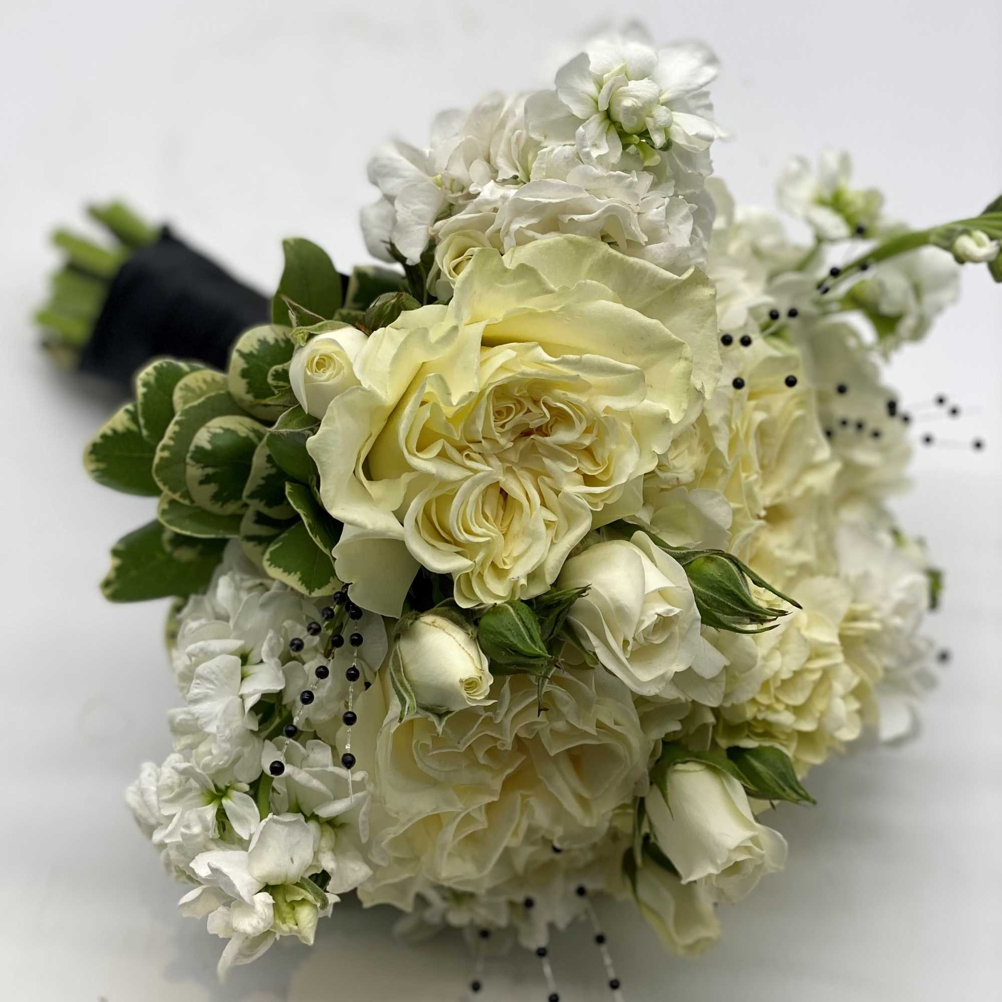 Hand-tied bouquet of ivory roses and white flowers with black bead accents and wrapped stems