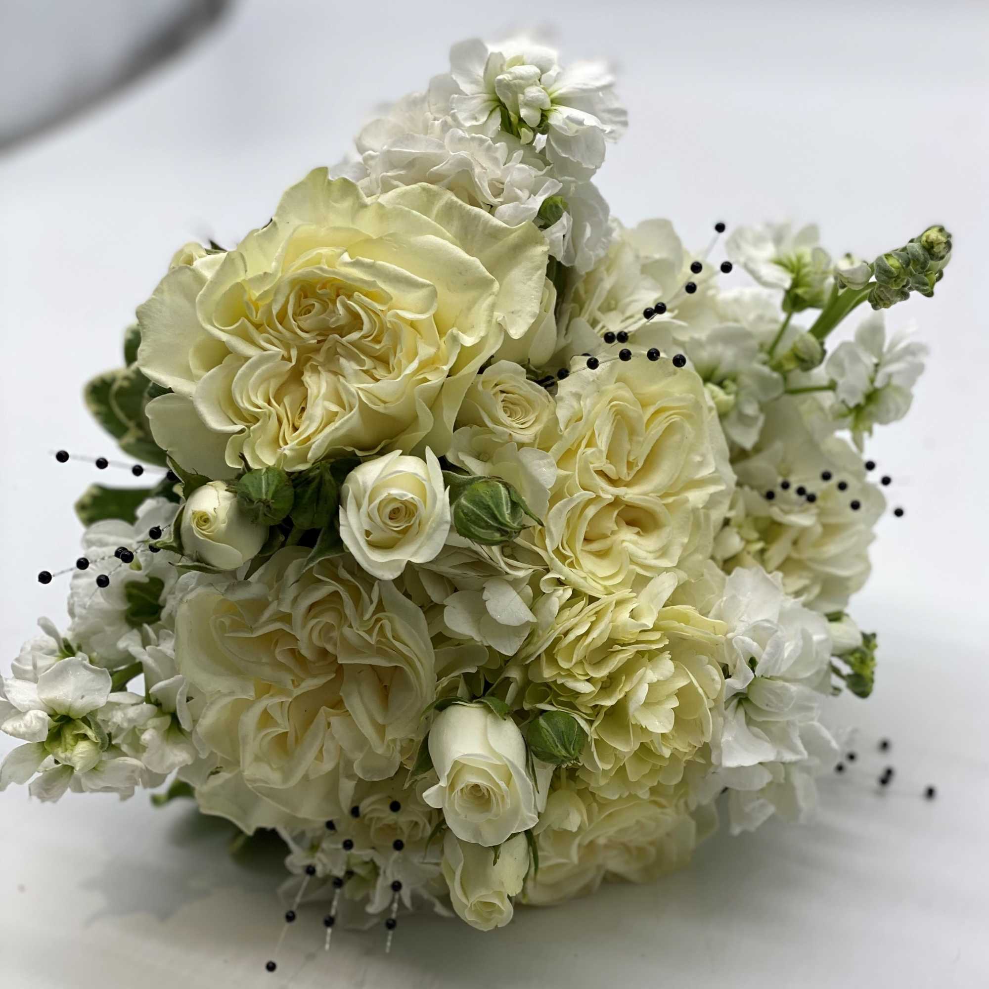A lush mix of white flowers accented with black pearl sprays with
