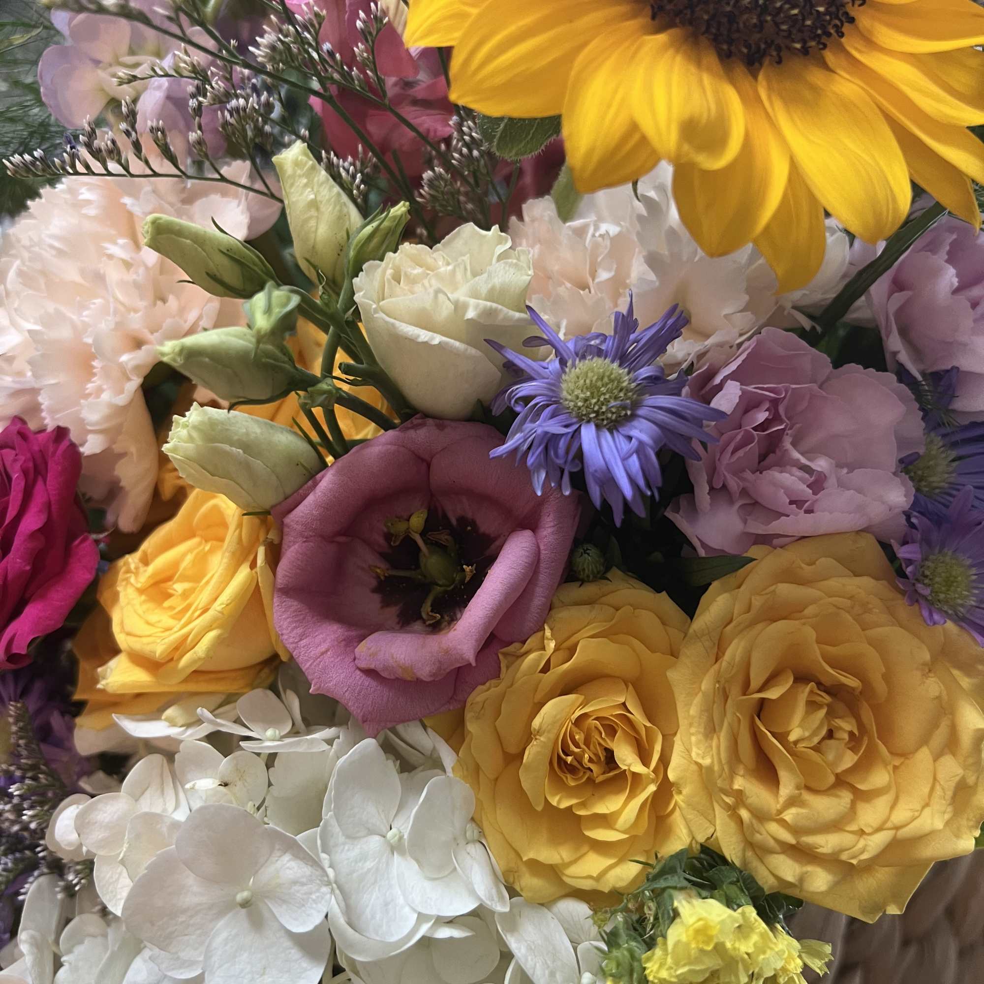 A vibrant and cheerful bouquet in a vase featuring sunflowers, spray roses