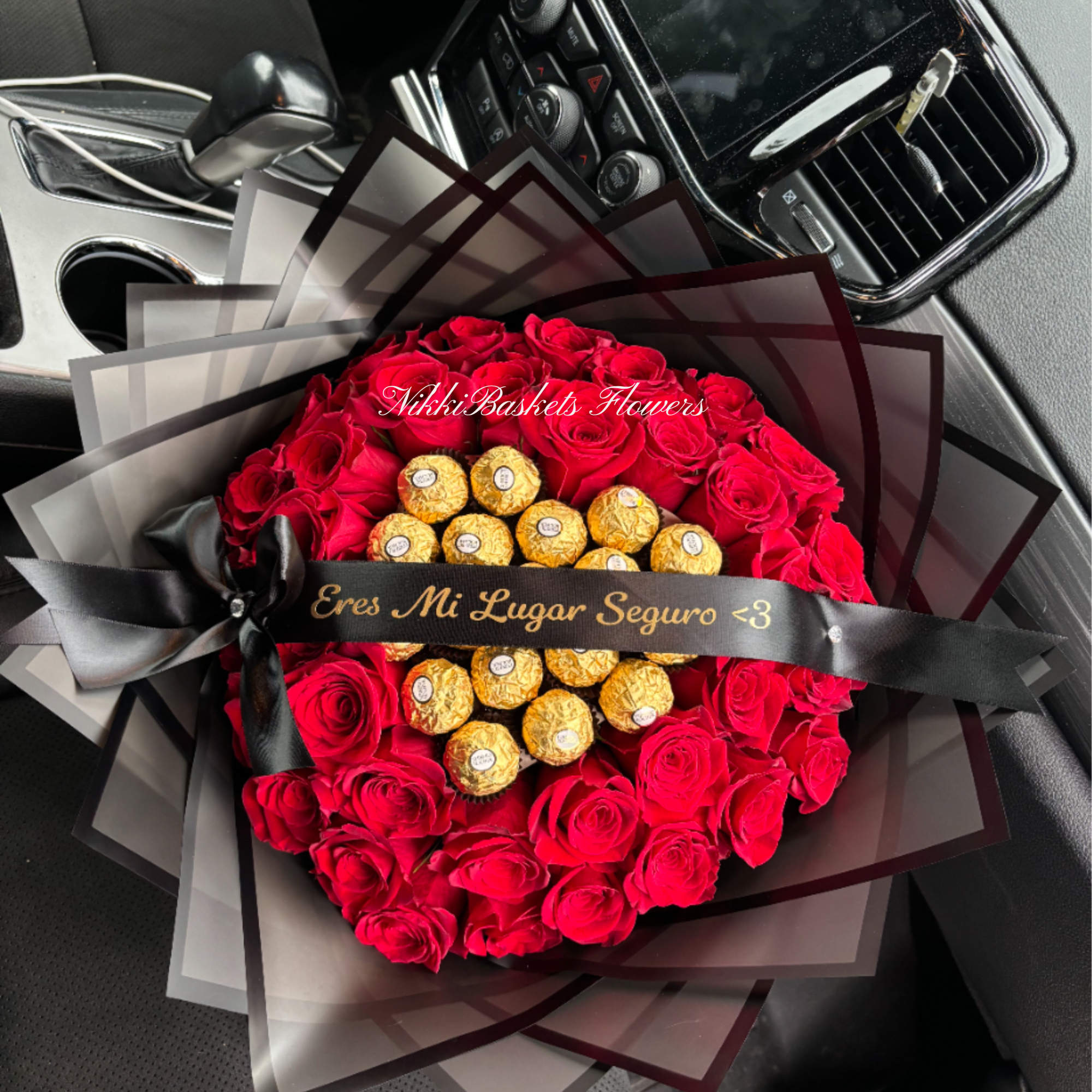 Round bouquet of red roses with gold-wrapped chocolates and black ribboned wrapping on a car seat.