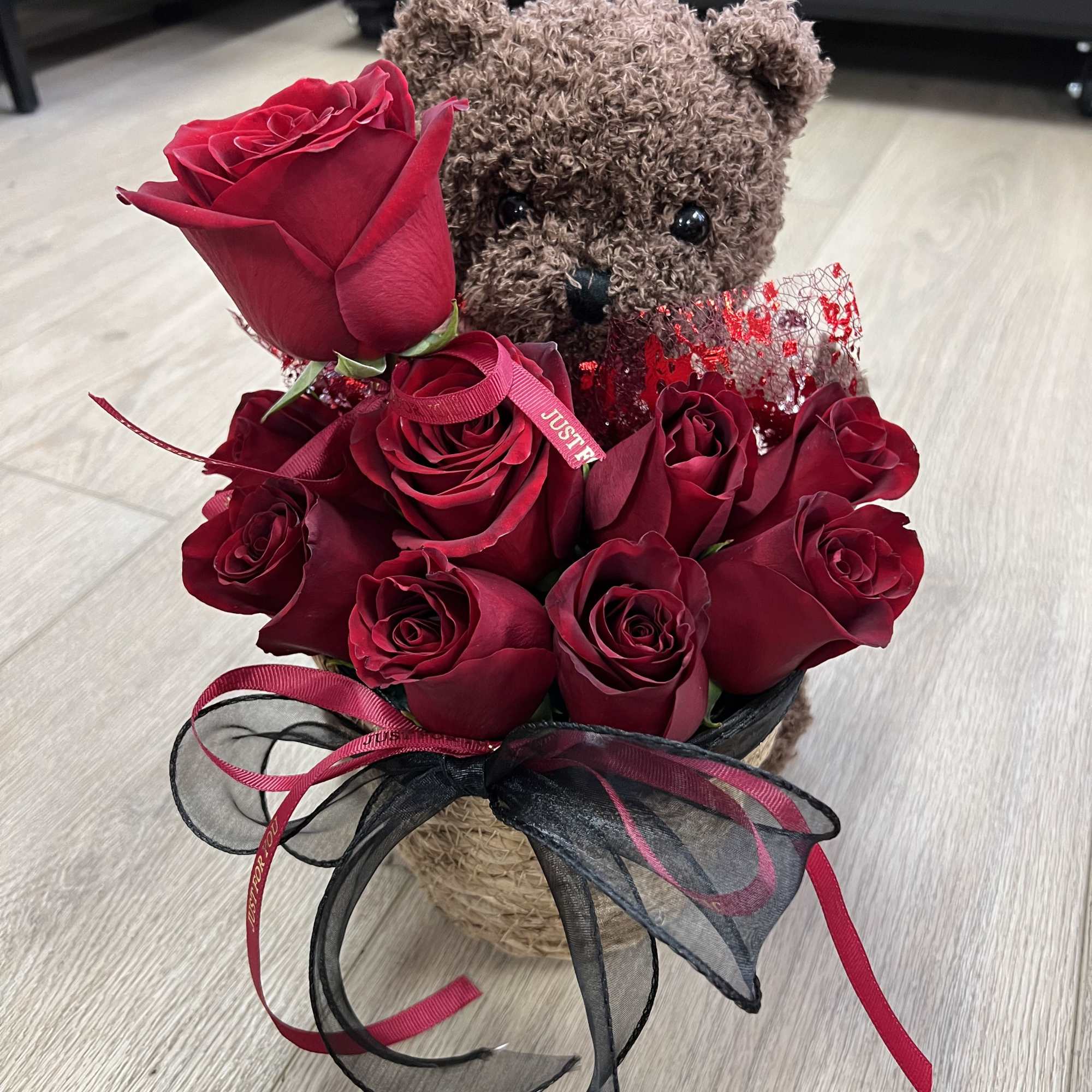 A charming teddy bear holding a bouquet of vibrant red roses adorned
