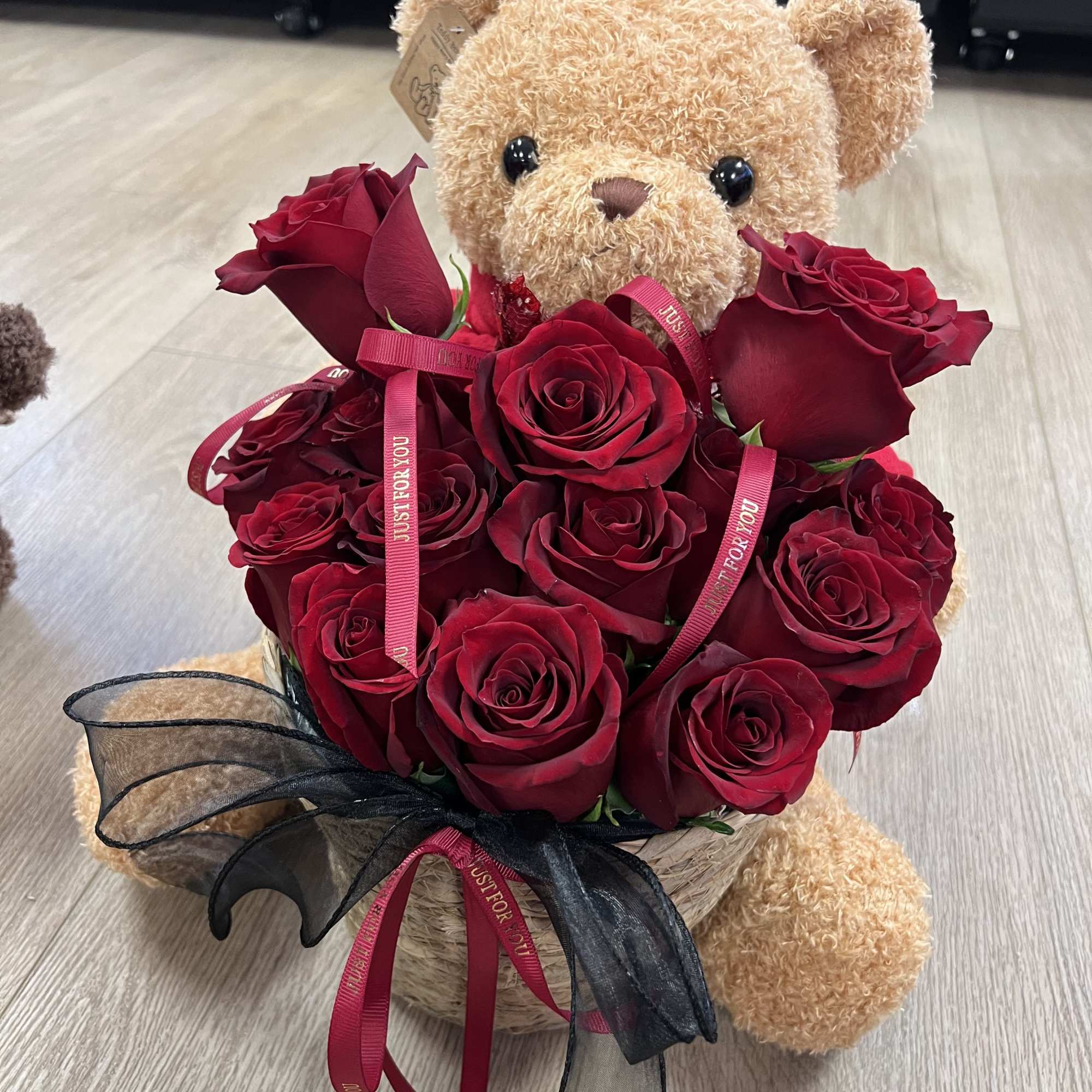 A charming teddy bear holding a bouquet of vibrant red roses adorned