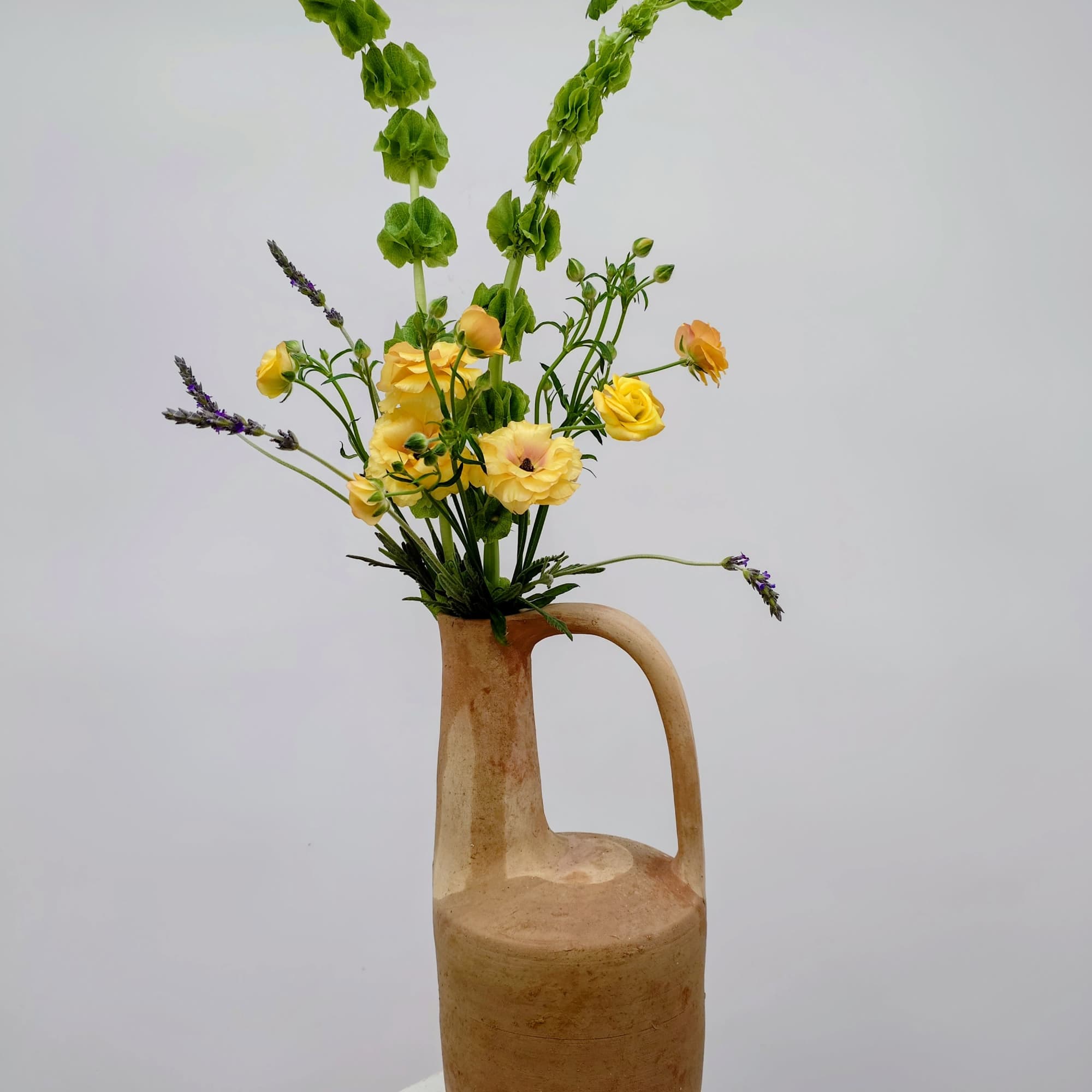 A sculptural floral arrangement designed in a tall, long-necked clay pitcher, Juno