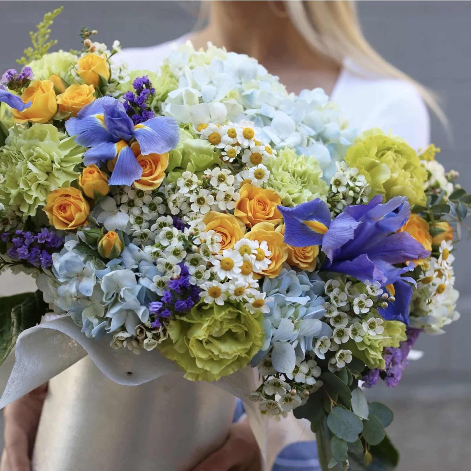 Large bouquet of blue, yellow, and green flowers held by a person