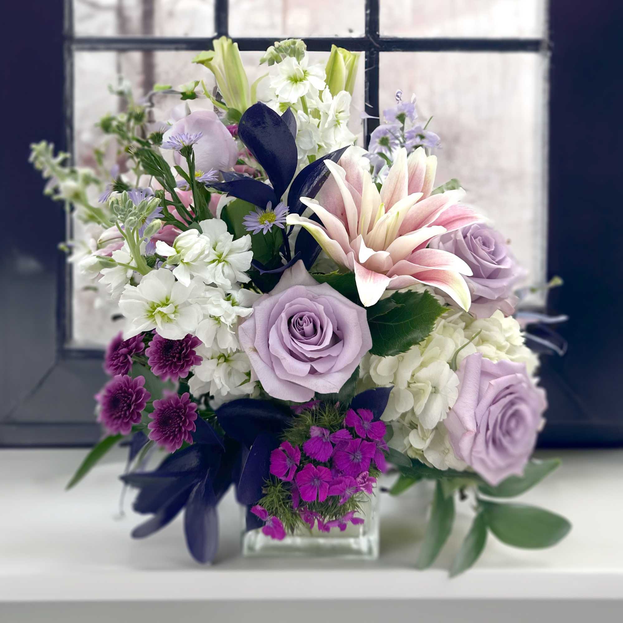 Roses, lilies, and mums in varying hues of purples and lavender.