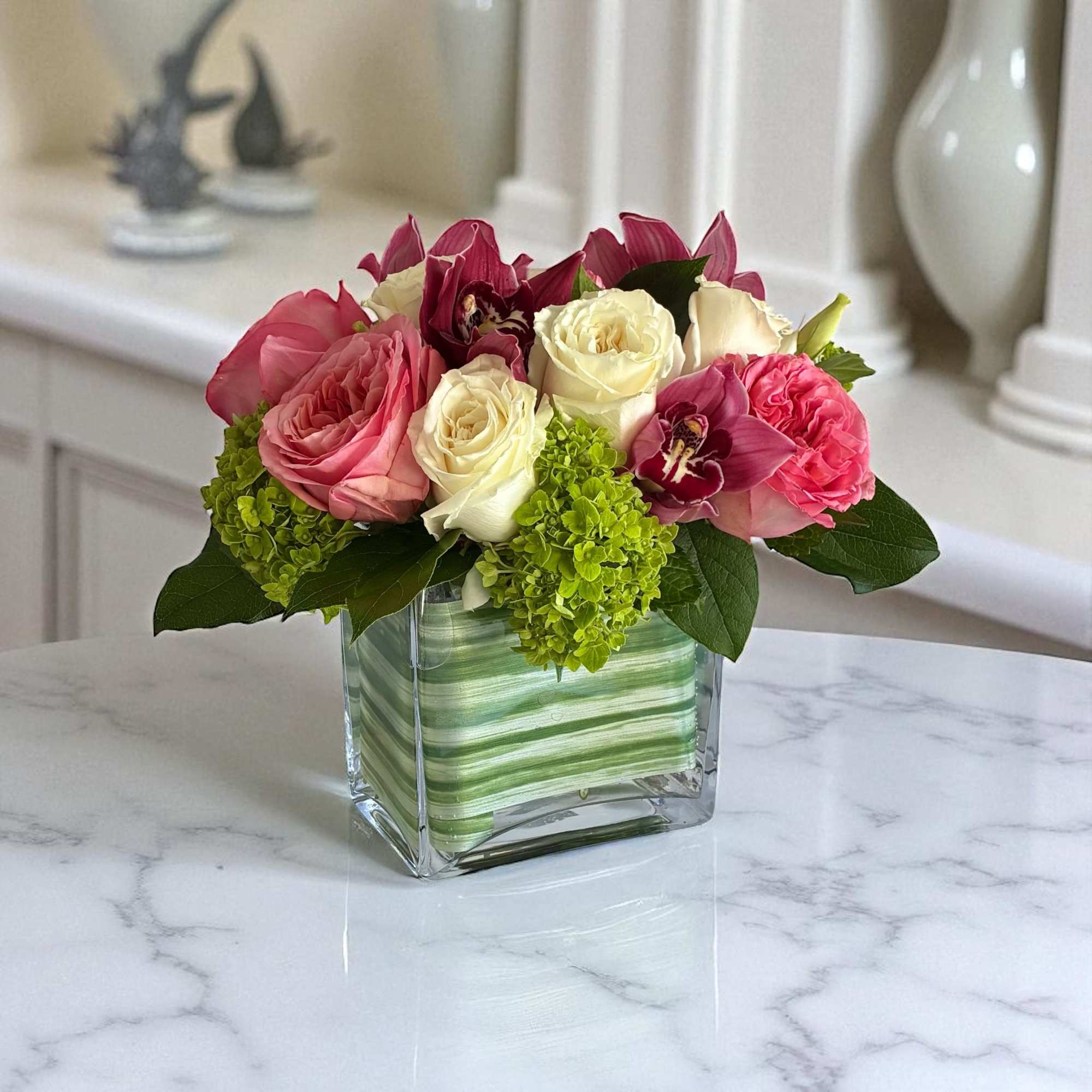 Pink and white roses in a square glass vase with green blooms