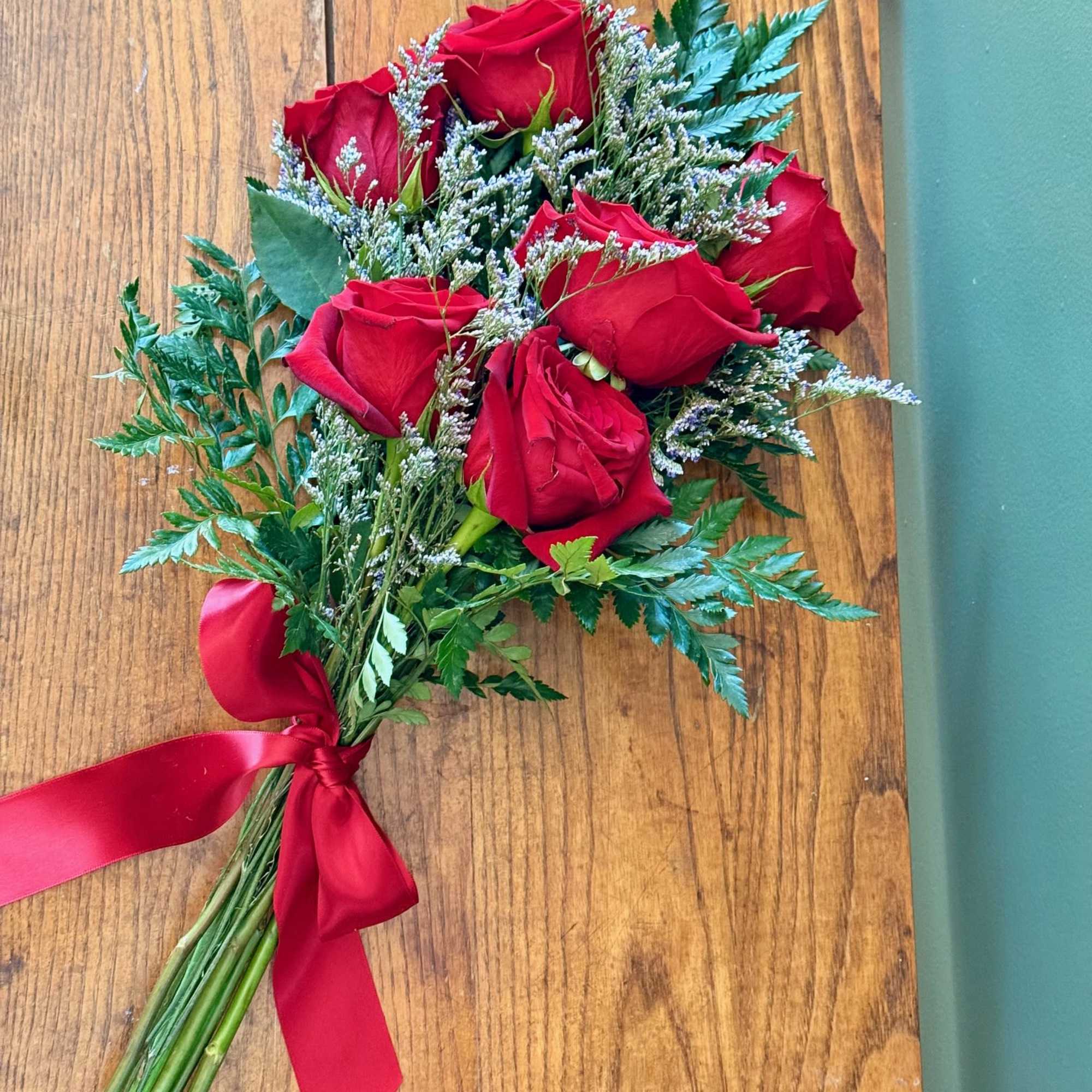 6 red roses with greenery wrapped in white or red ribbon. 
Add