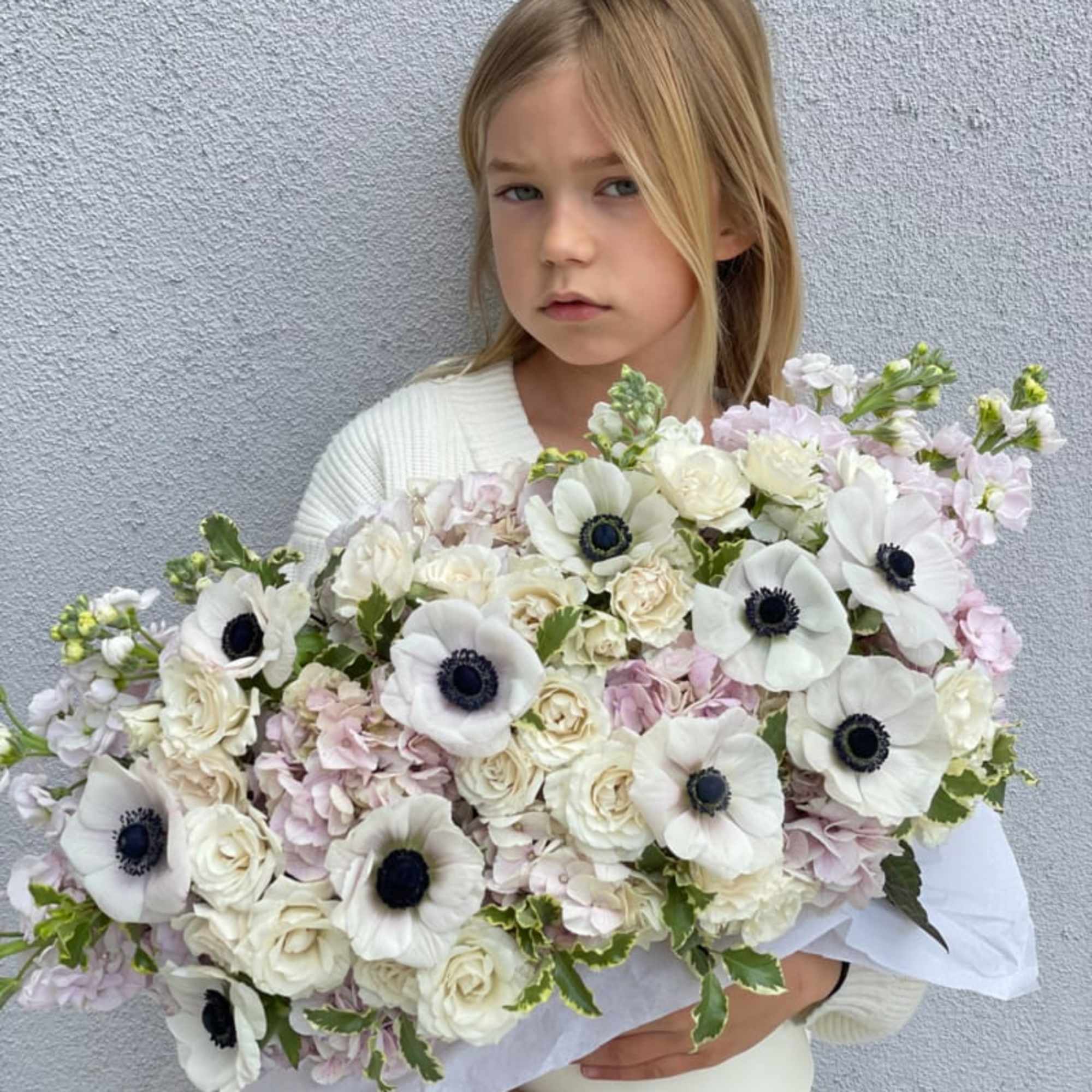 Child holding a large bouquet of white and pale pink flowers