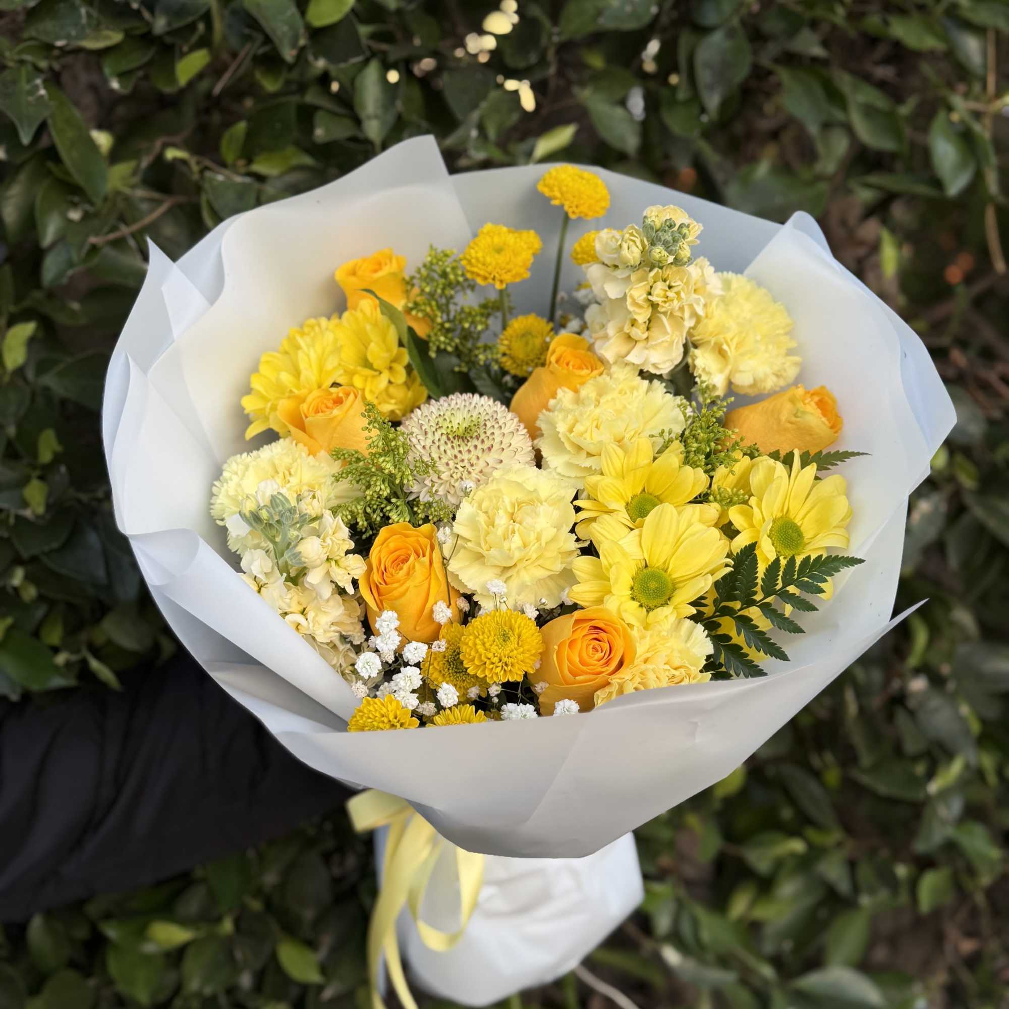 A bright wrapped handheld bouquet of yellow roses and seasonal blooms, accented