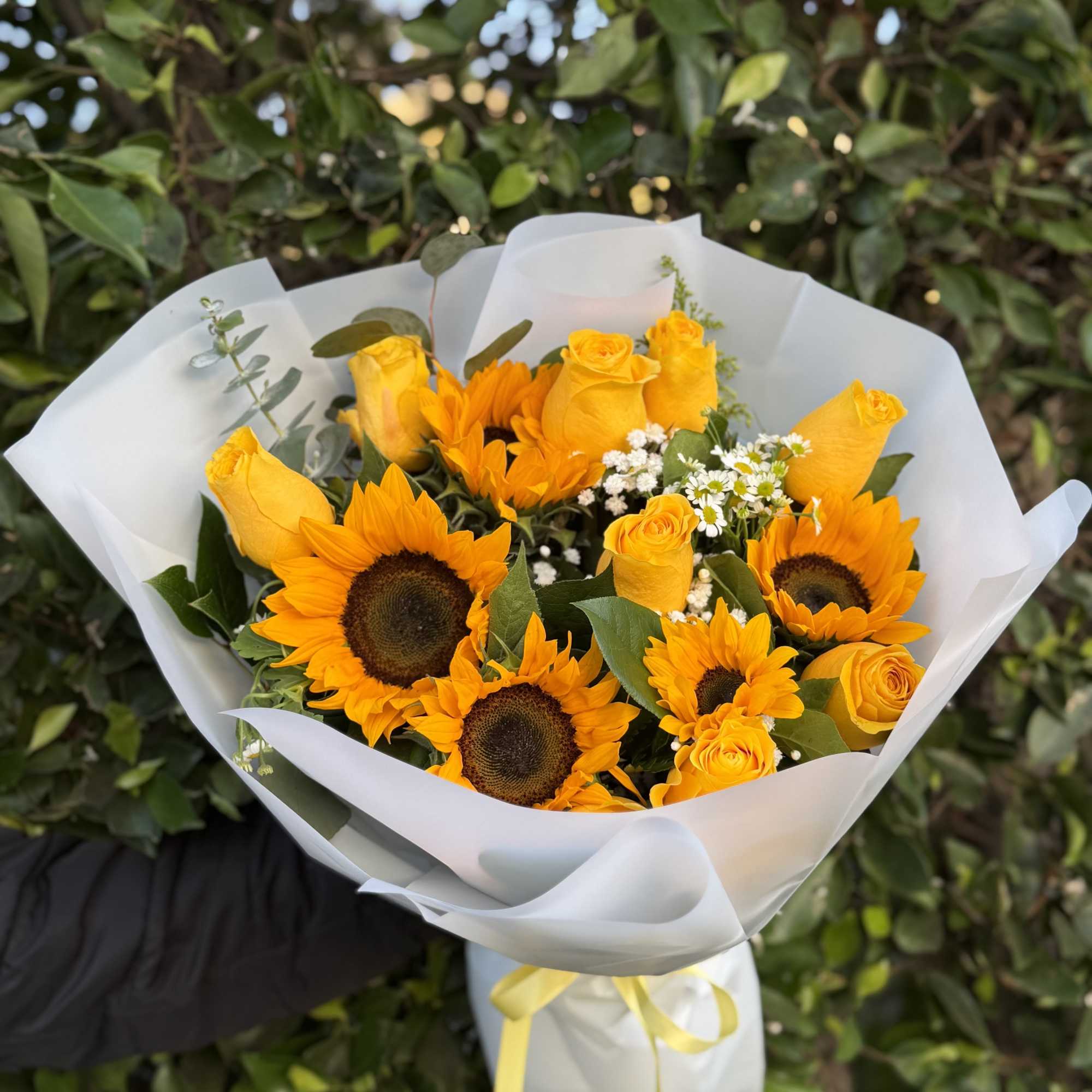 A radiant wrapped handheld bouquet of sunflowers and yellow roses, accented with