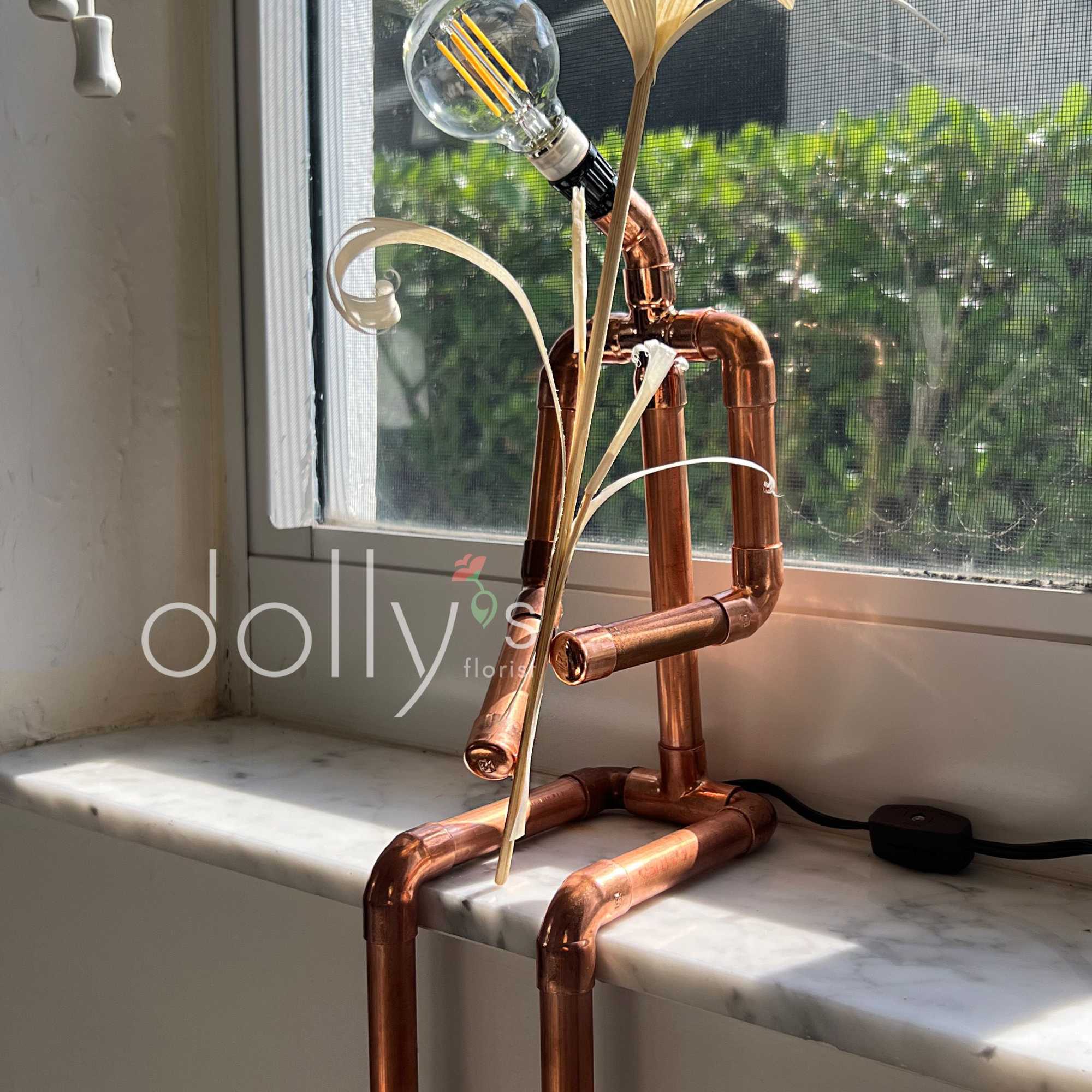 Copper pipe lamp with a light bulb and dried palm leaves on a windowsill