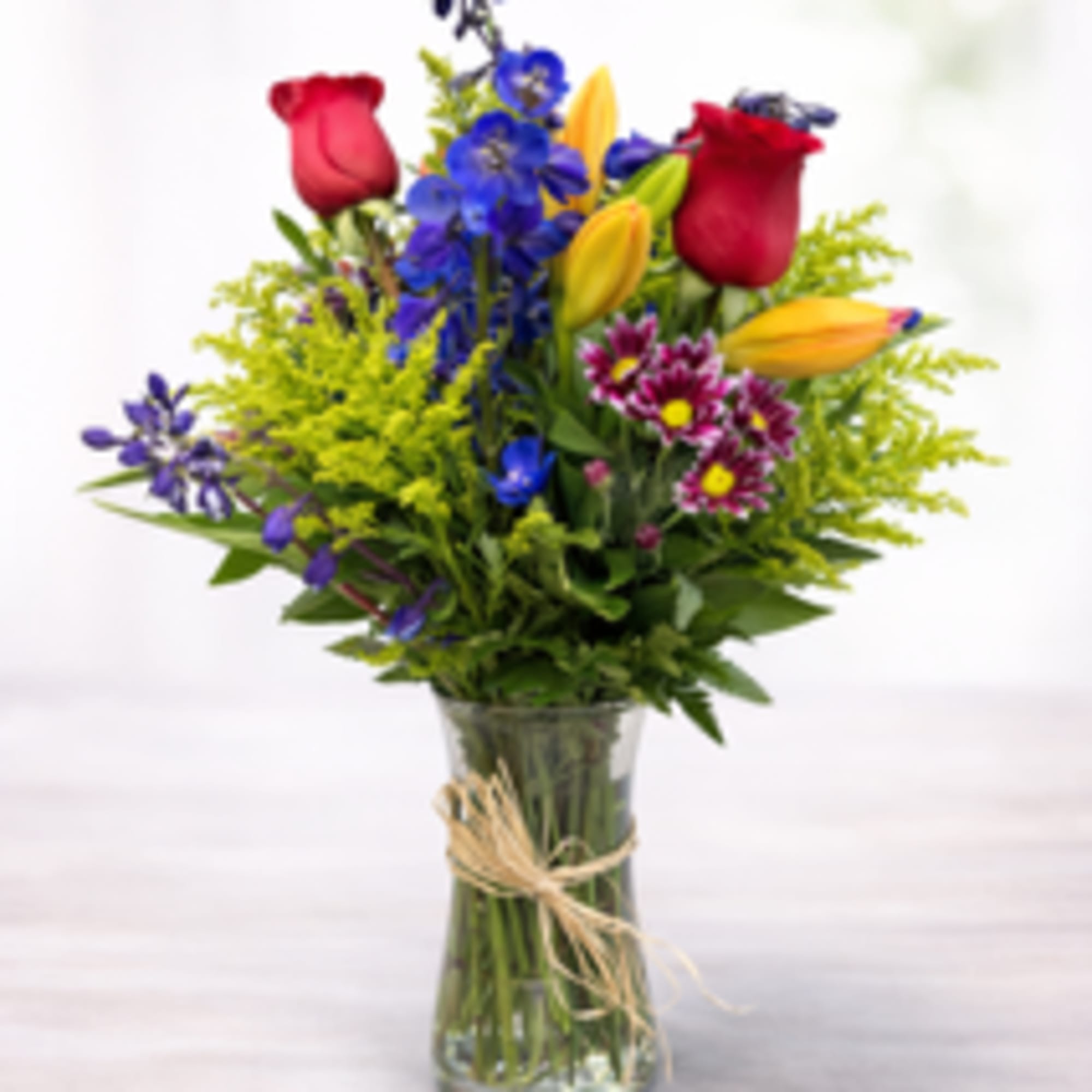 Mixed bouquet of roses, lilies, and blue flowers in a glass vase