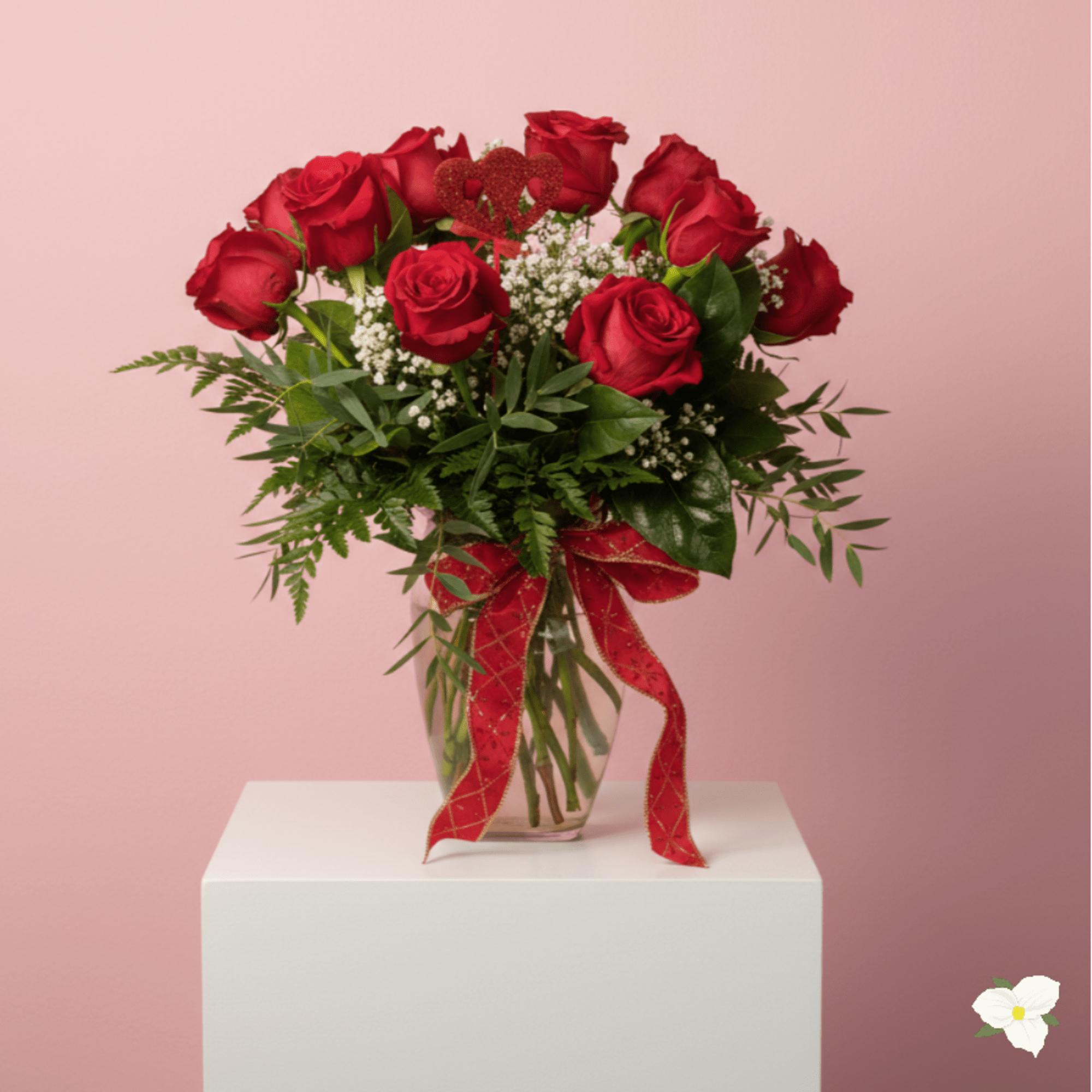 Arrangement of red roses with white filler flowers and a red bow in a clear glass vase