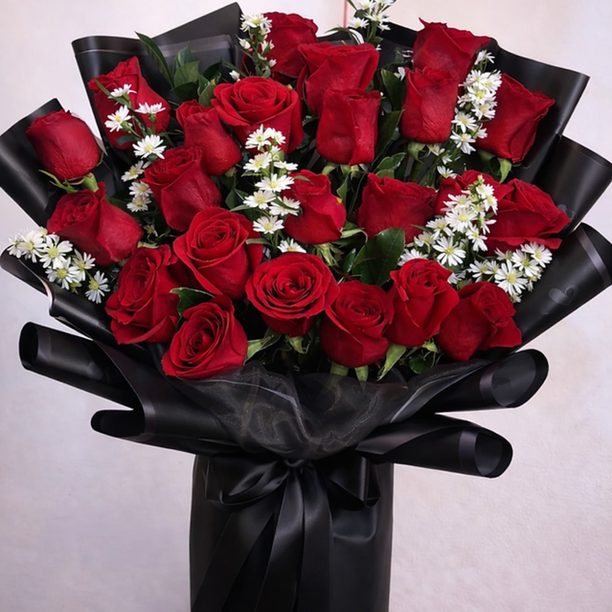 A lush cluster of deep red roses framed by crisp white daisy-like