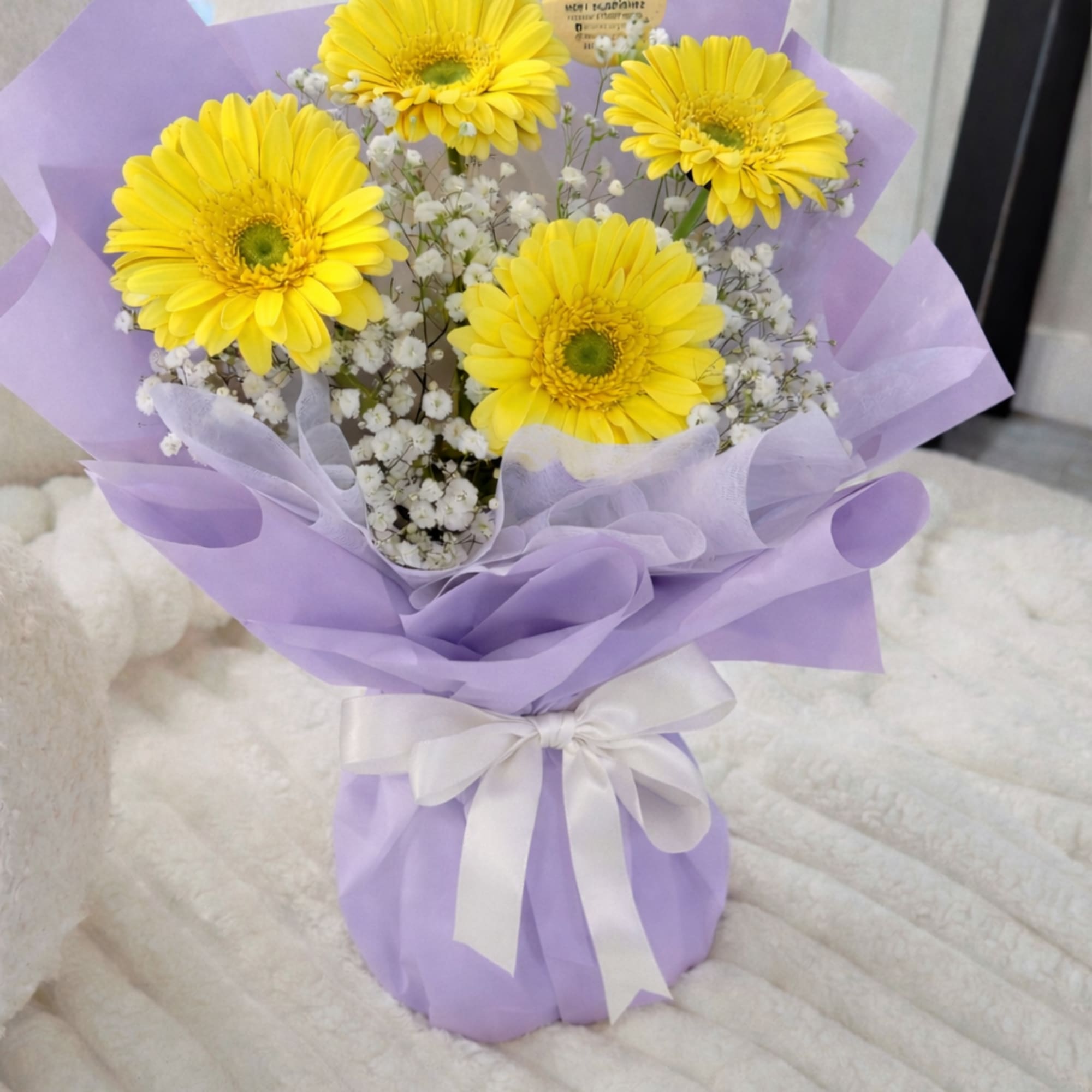 A cheerful arrangement of fresh yellow gerberas with delicate baby&rsquo;s breath, wrapped