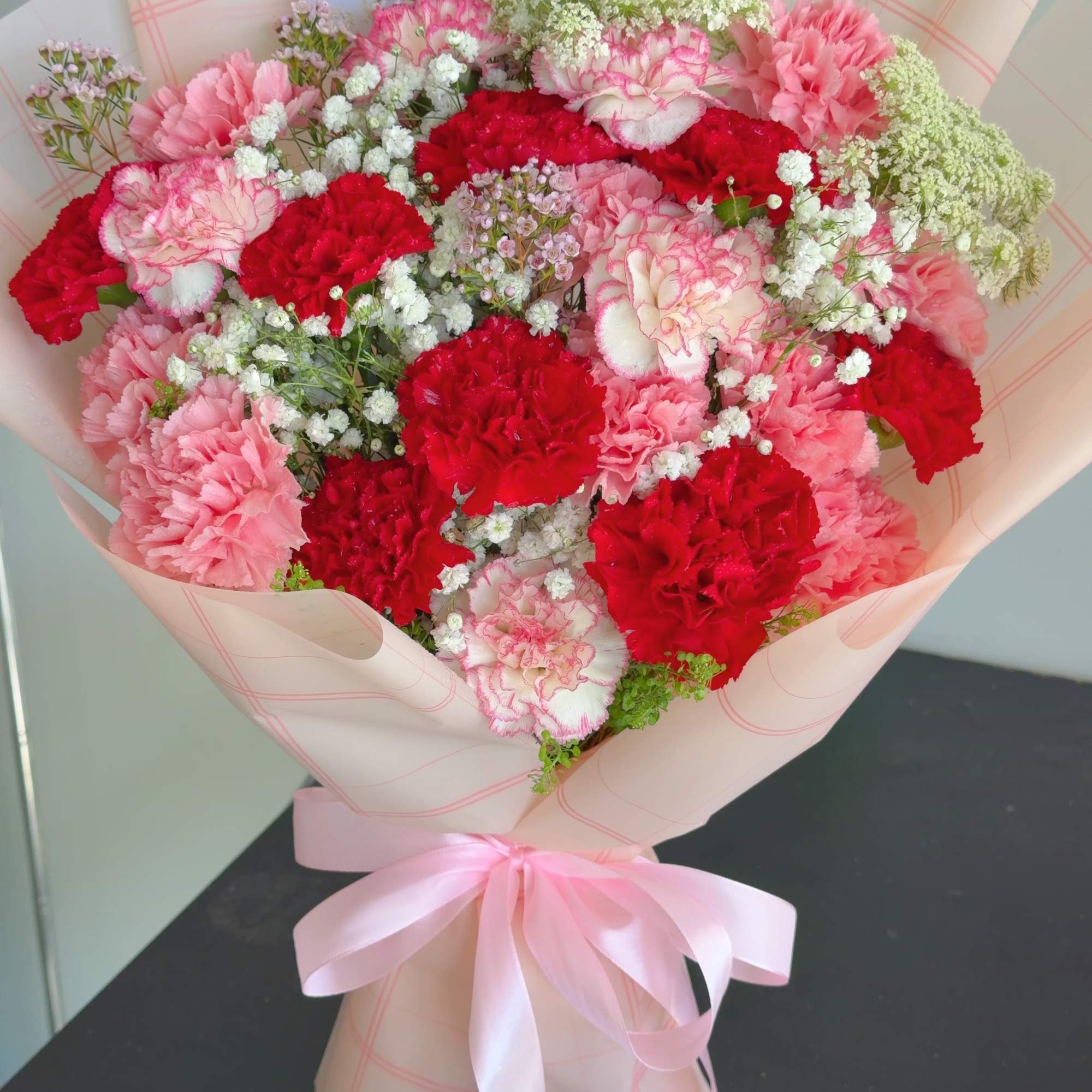 The product contains red and pink carnations with green leafy flowers and