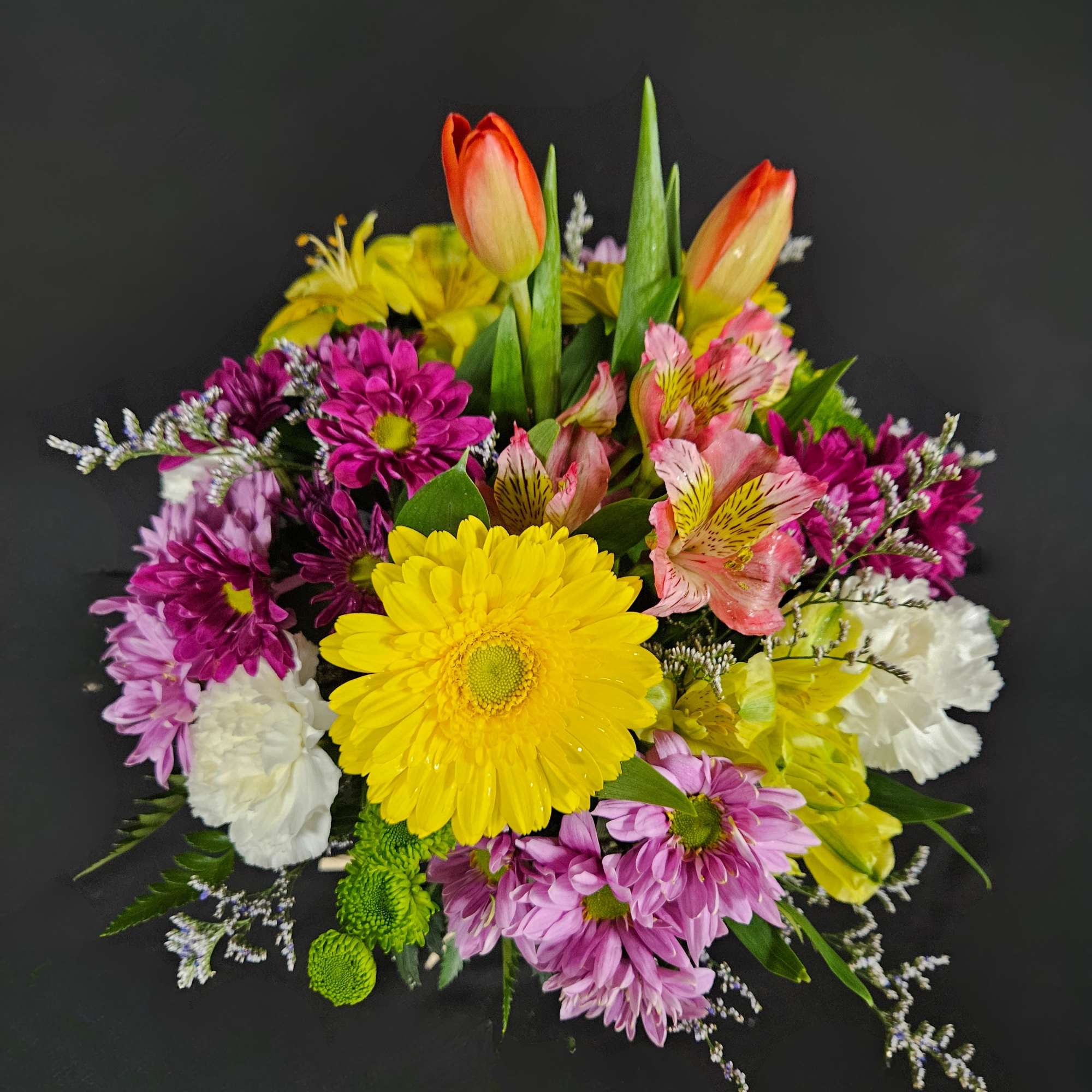 This mason jar is filled with tulips, spring colored gerbera daisies, carnations