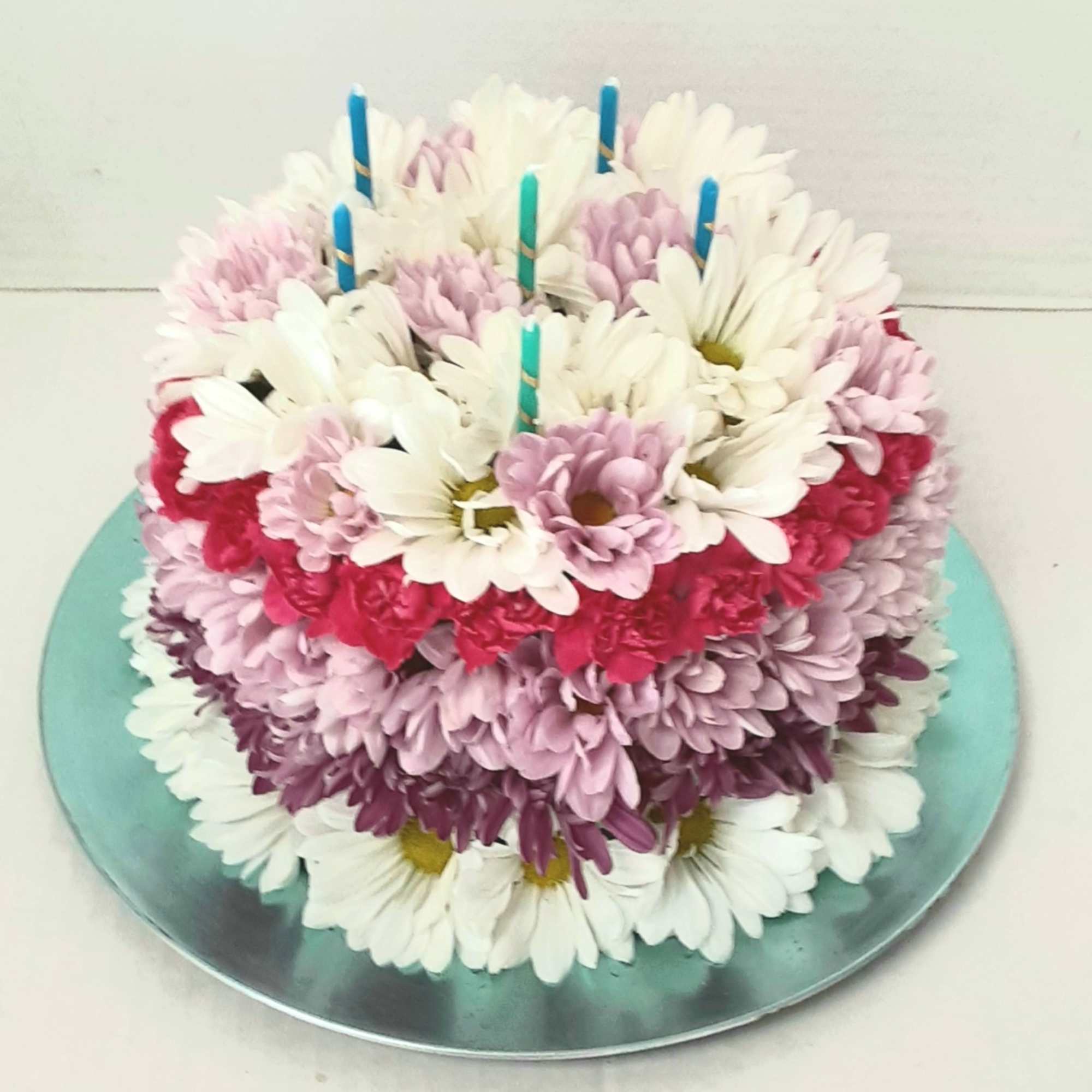 Round cake covered with white, pink, and purple daisies and candles on top