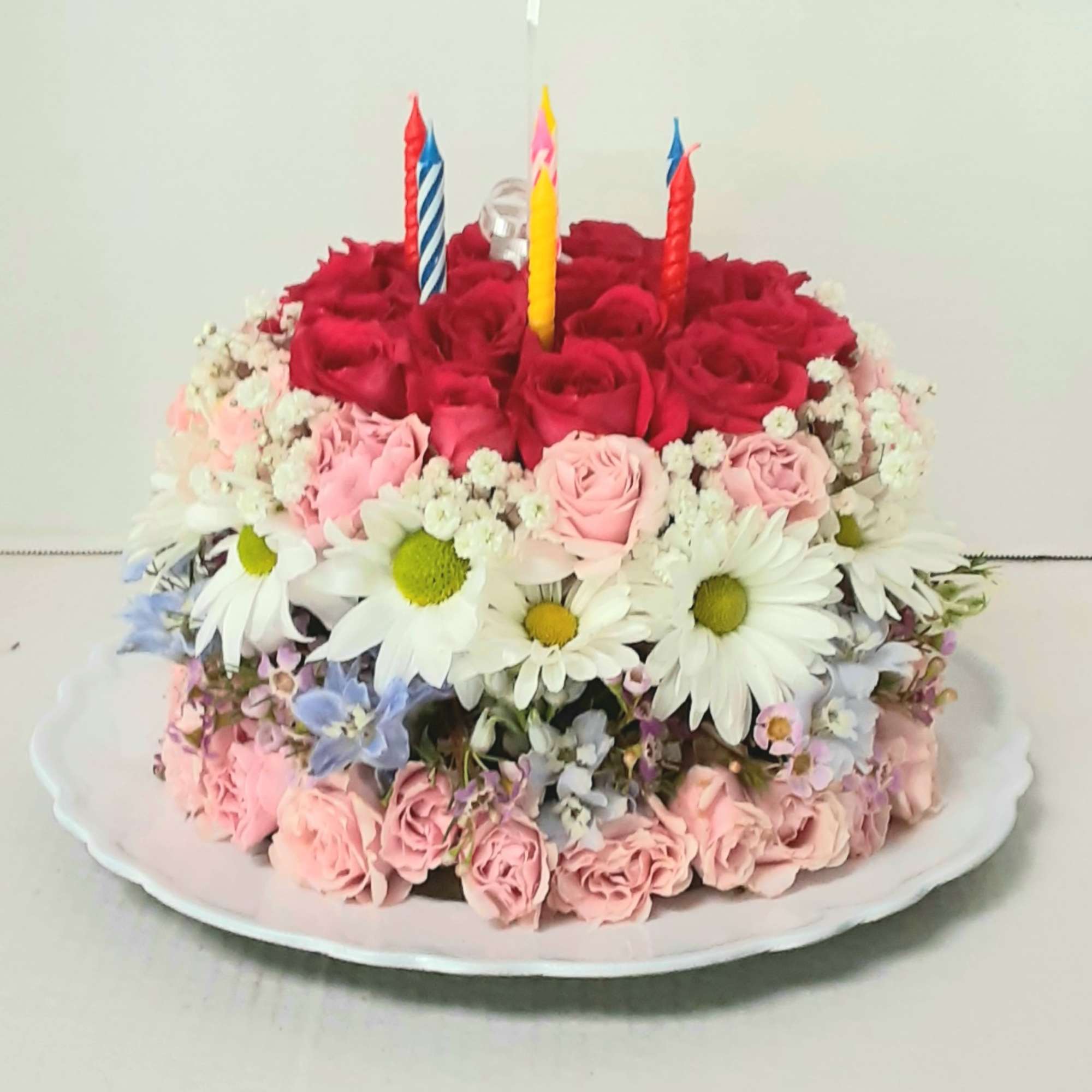 Round floral cake with candles on a white platter