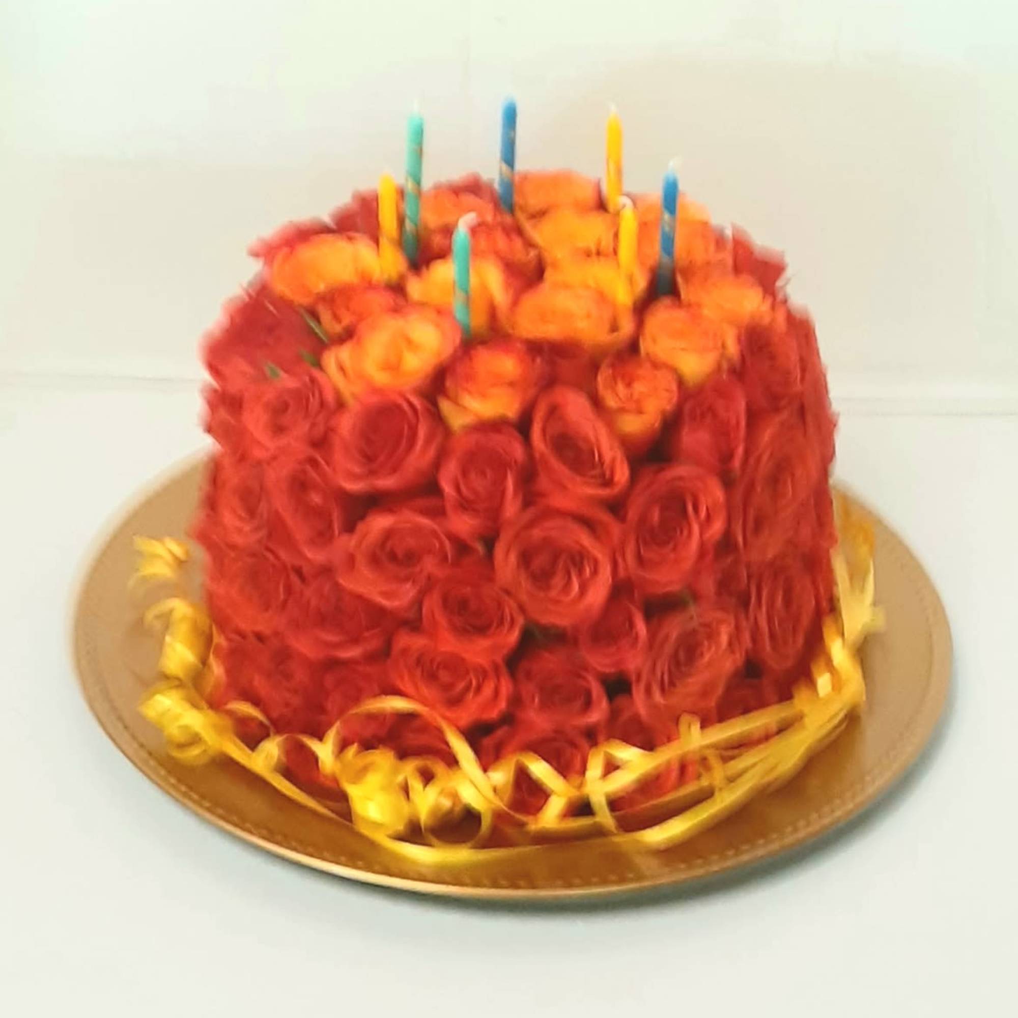 Round cake covered in red and orange roses with candles on top