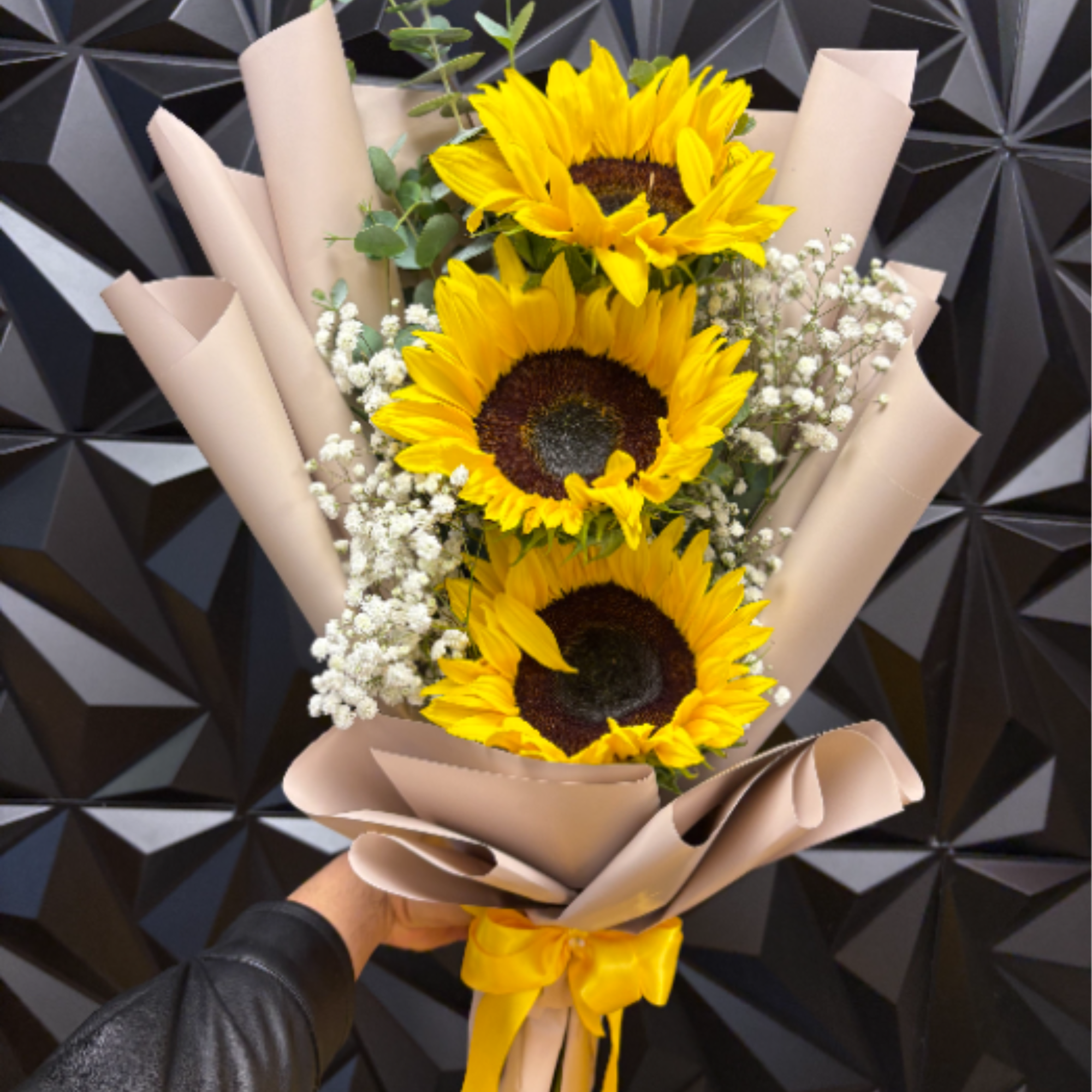 Wrapped bouquet of three yellow sunflowers with white filler flowers and a yellow ribbon.