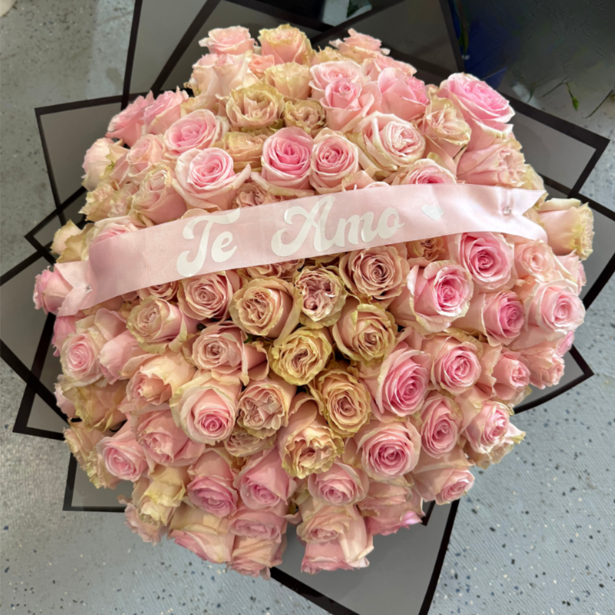 100 Red Roses Wrapped in black paper with a ribbon Saying I