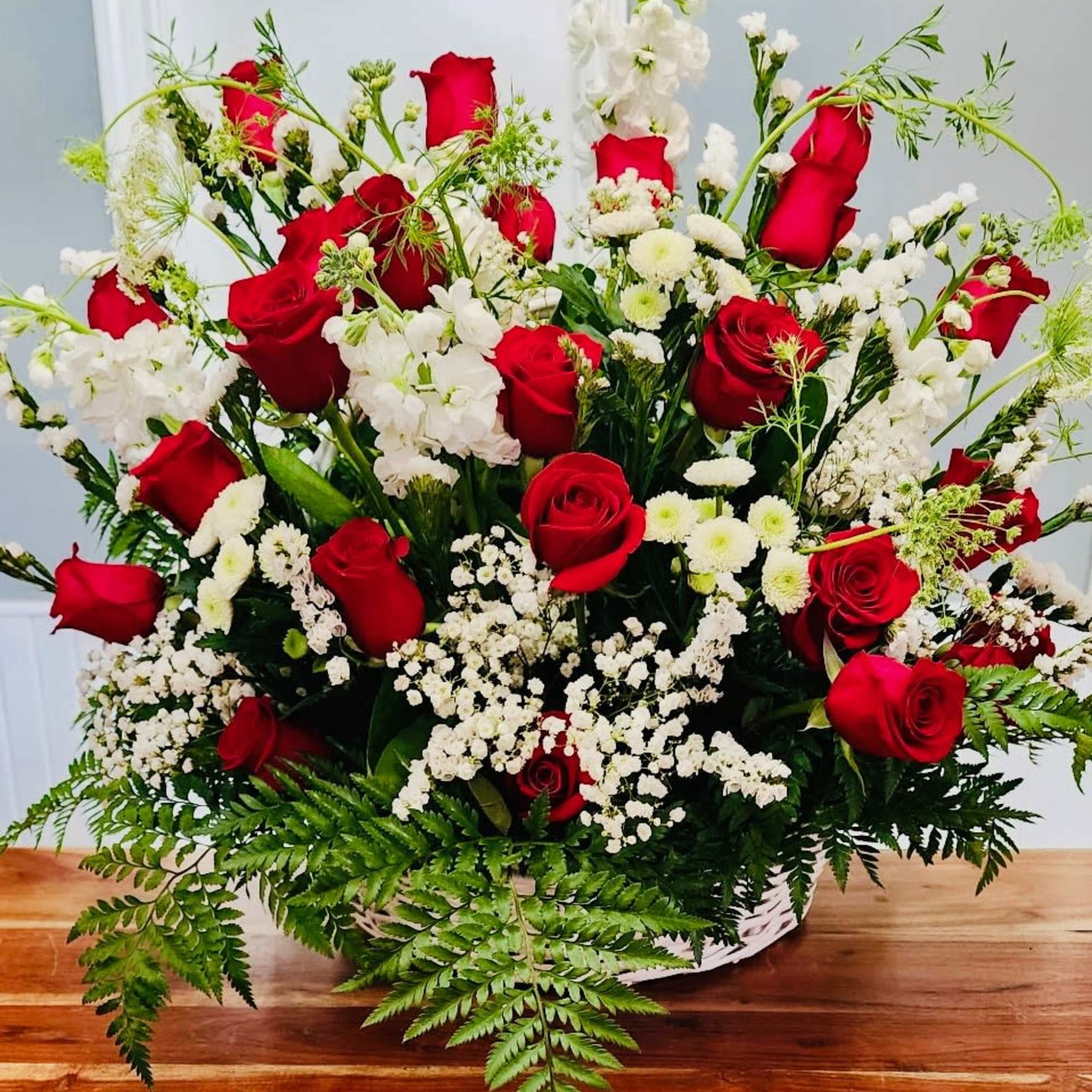 Large arrangement of red roses and white flowers in a low white basket.