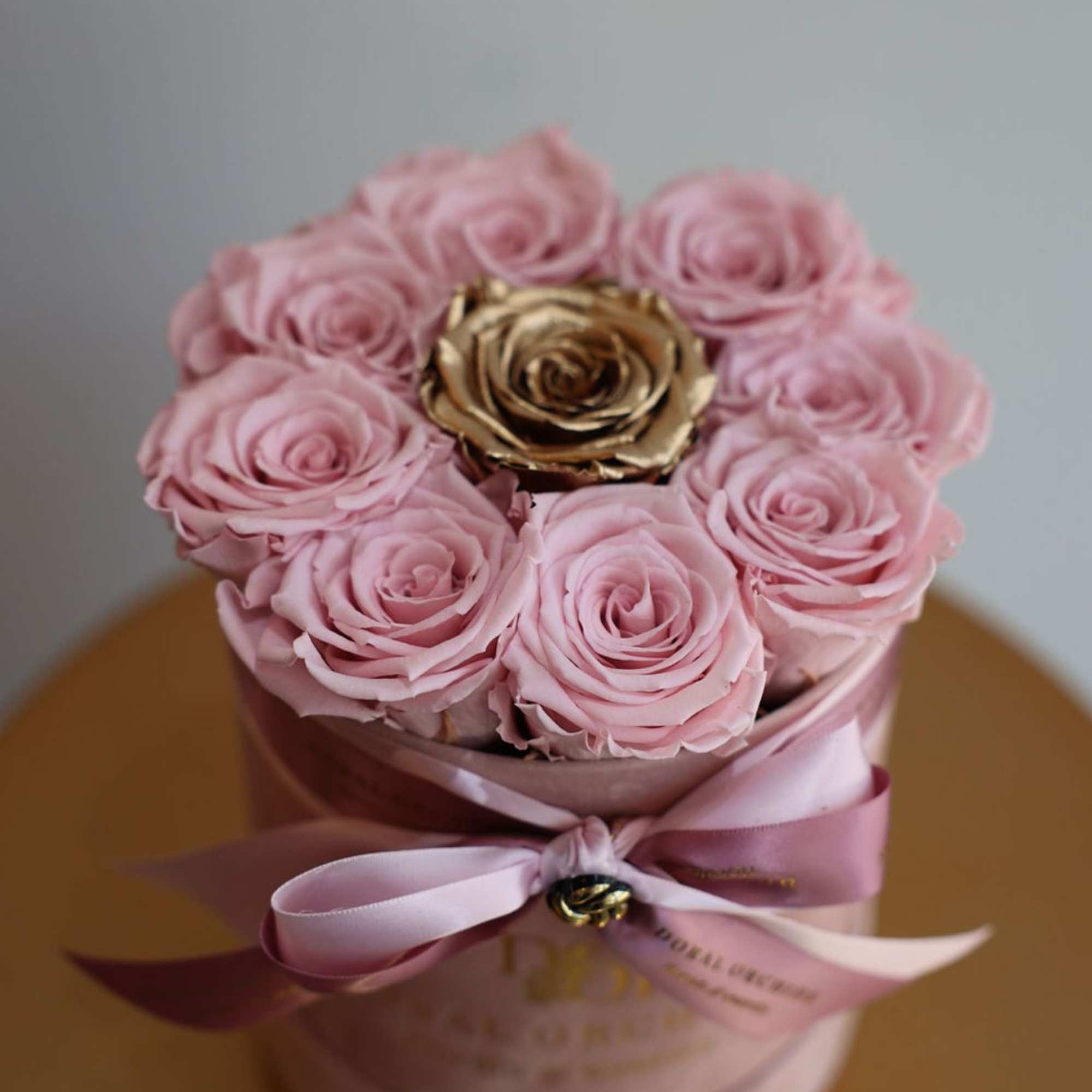 Soft preserved pink roses surround a single radiant gold rose at the