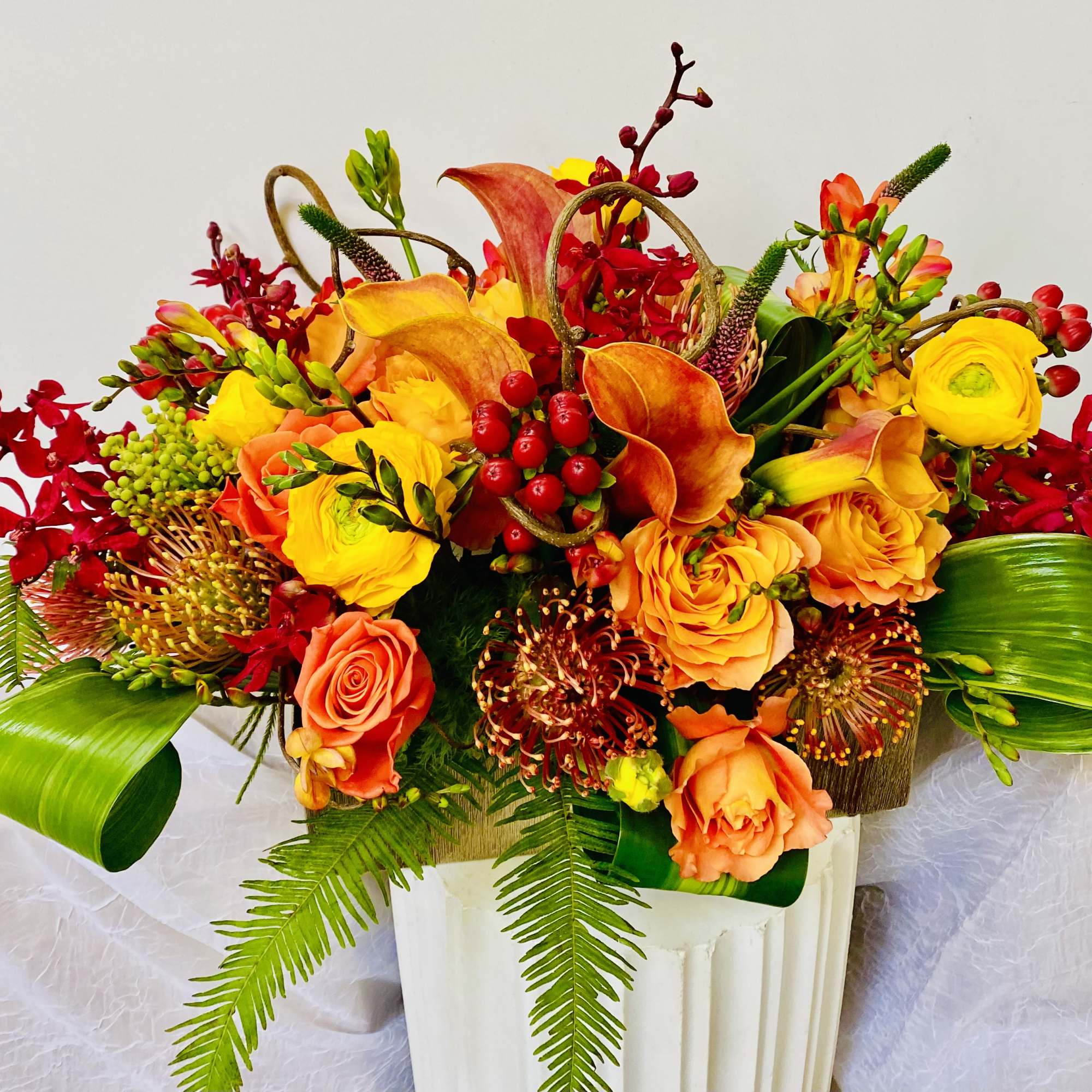 In a long vase combination of red roses, yellow roses, burgundy orchids