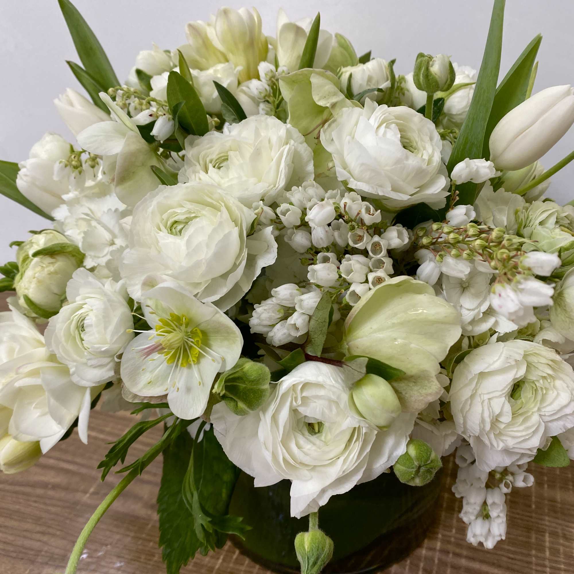 White Hydrangea, tulips, ranunculus in 
a clear glass vase.